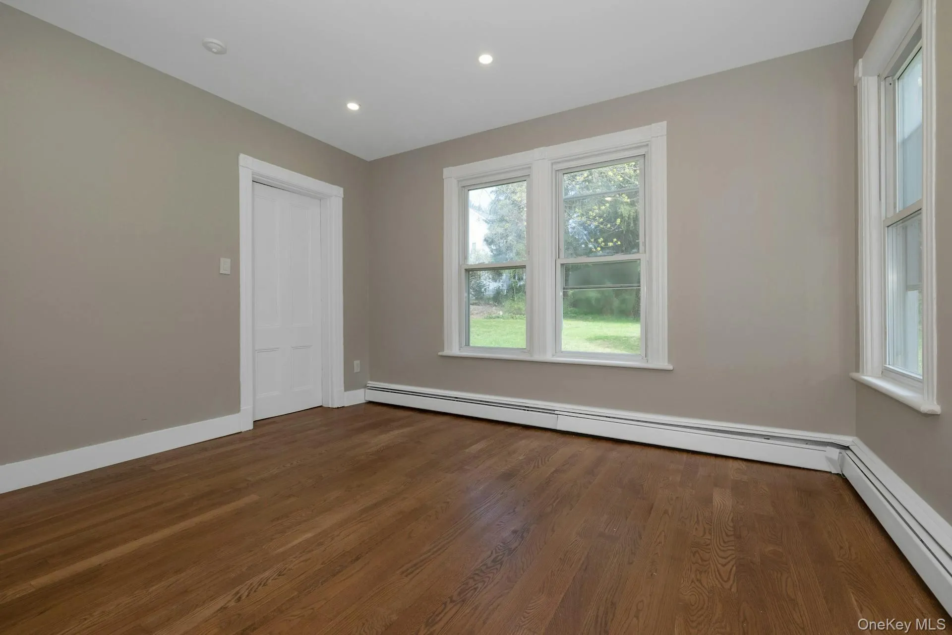 Empty room featuring baseboard heating, dark wood-style floors, and recessed lighting Empty room featuring baseboard heating, dark wood-style floors, and recessed lighting