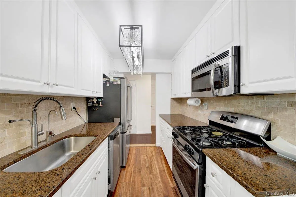 Kitchen featuring appliances with stainless steel finishes, light wood-type flooring, white cabinetry, decorative backsplash, and dark stone counters Kitchen featuring appliances with stainless steel finishes, light wood-type flooring, white cabinetry, decorative backsplash, and dark stone counters