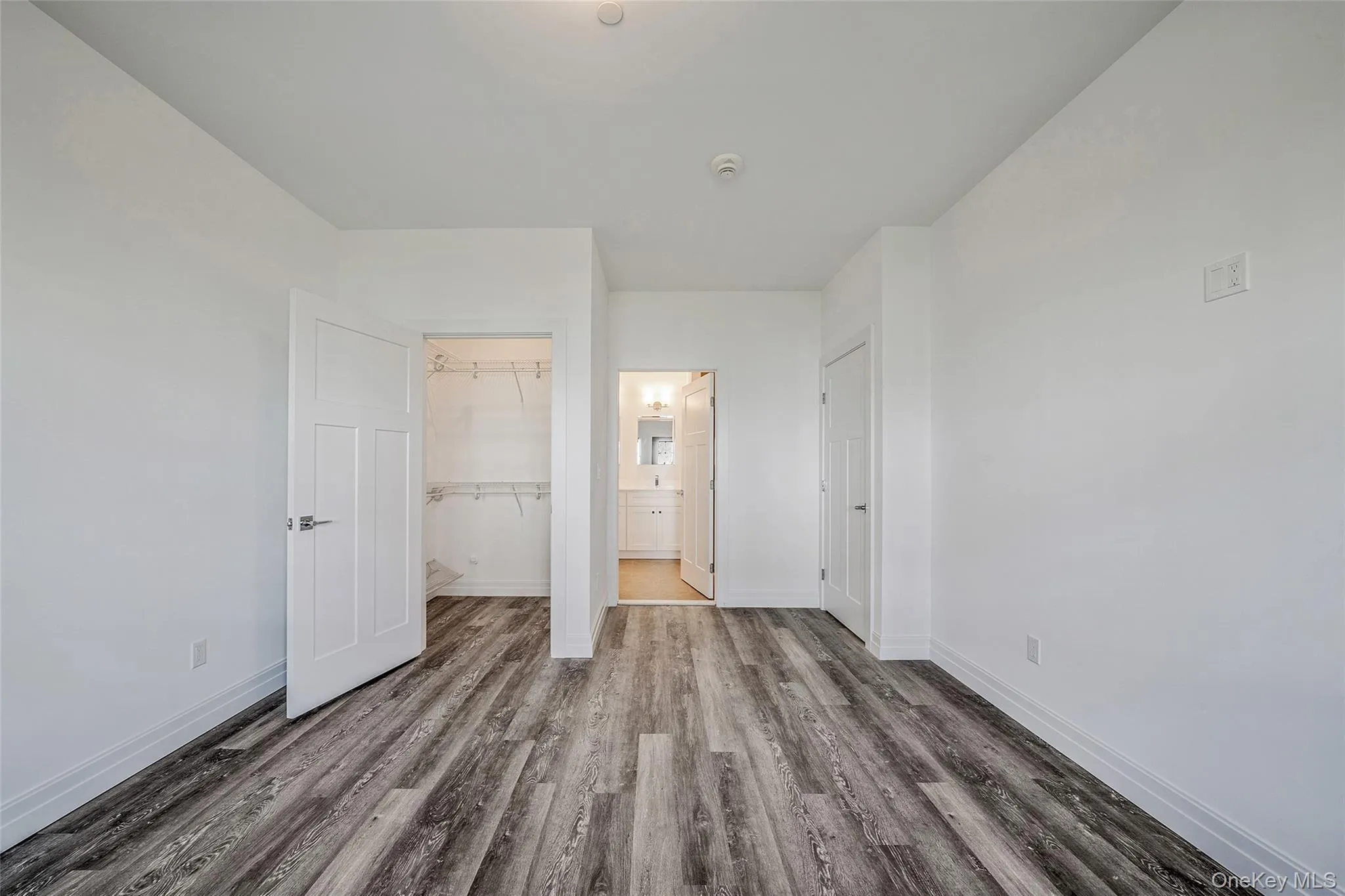 Unfurnished bedroom featuring wood finished floors, a spacious closet, and ensuite bath Unfurnished bedroom featuring wood finished floors, a spacious closet, and ensuite bath
