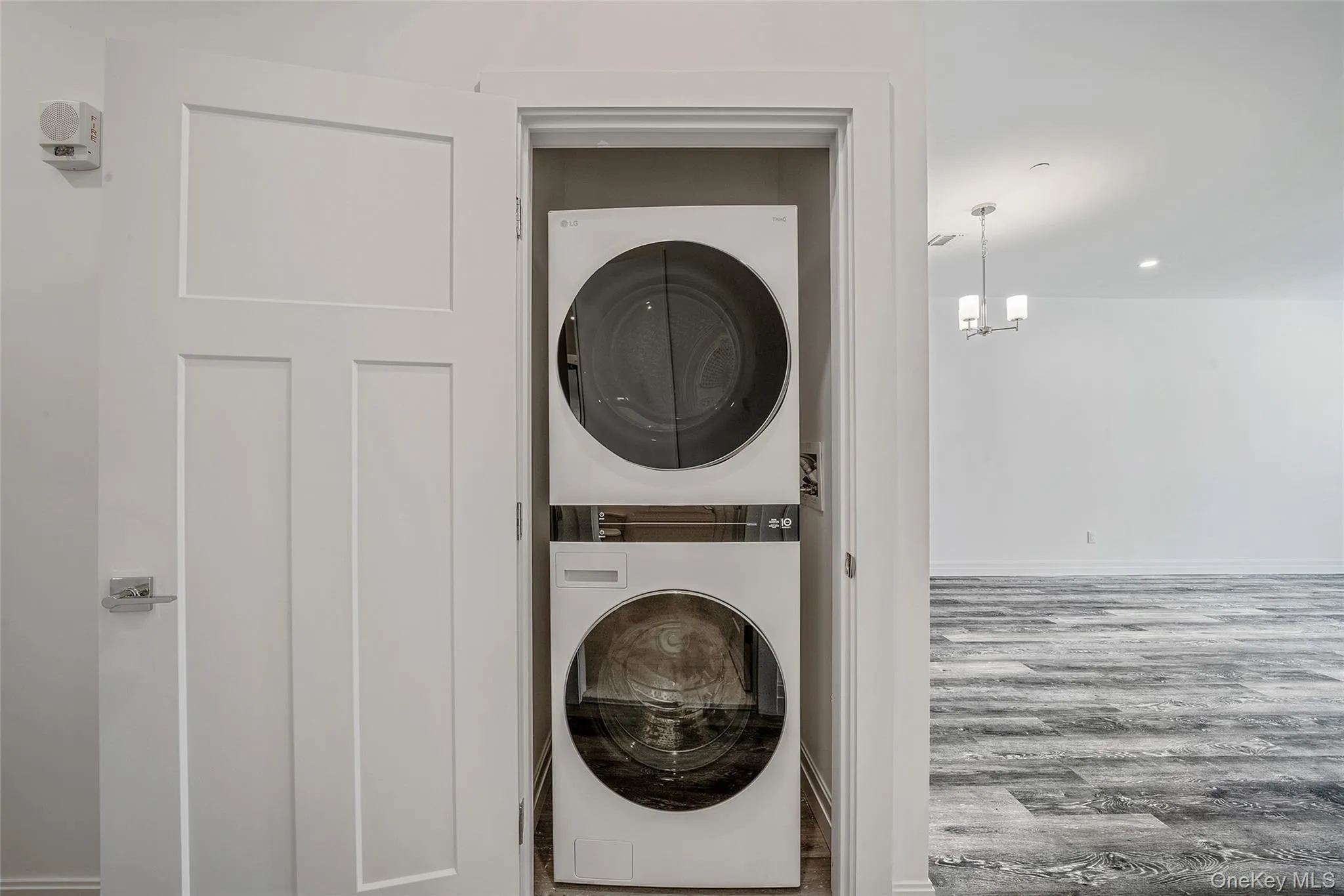 Laundry room featuring wood finished floors, stacked washer / drying machine, and a chandelier Laundry room featuring wood finished floors, stacked washer / drying machine, and a chandelier