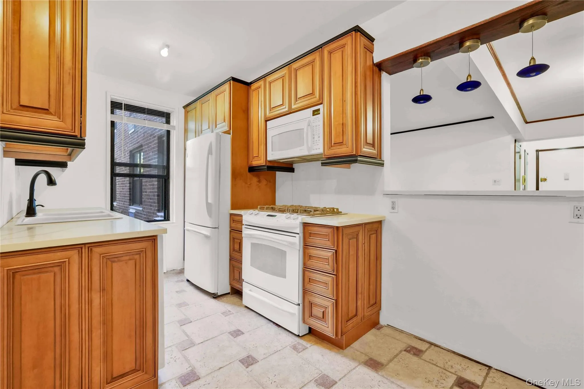 Kitchen with white appliances, brown cabinetry, and stone tile flooring Kitchen with white appliances, brown cabinetry, and stone tile flooring
