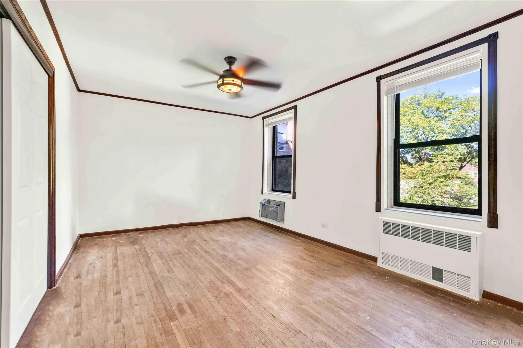 Unfurnished bedroom with crown molding, radiator, light wood-type flooring, ceiling fan, and a closet Unfurnished bedroom with crown molding, radiator, light wood-type flooring, ceiling fan, and a closet