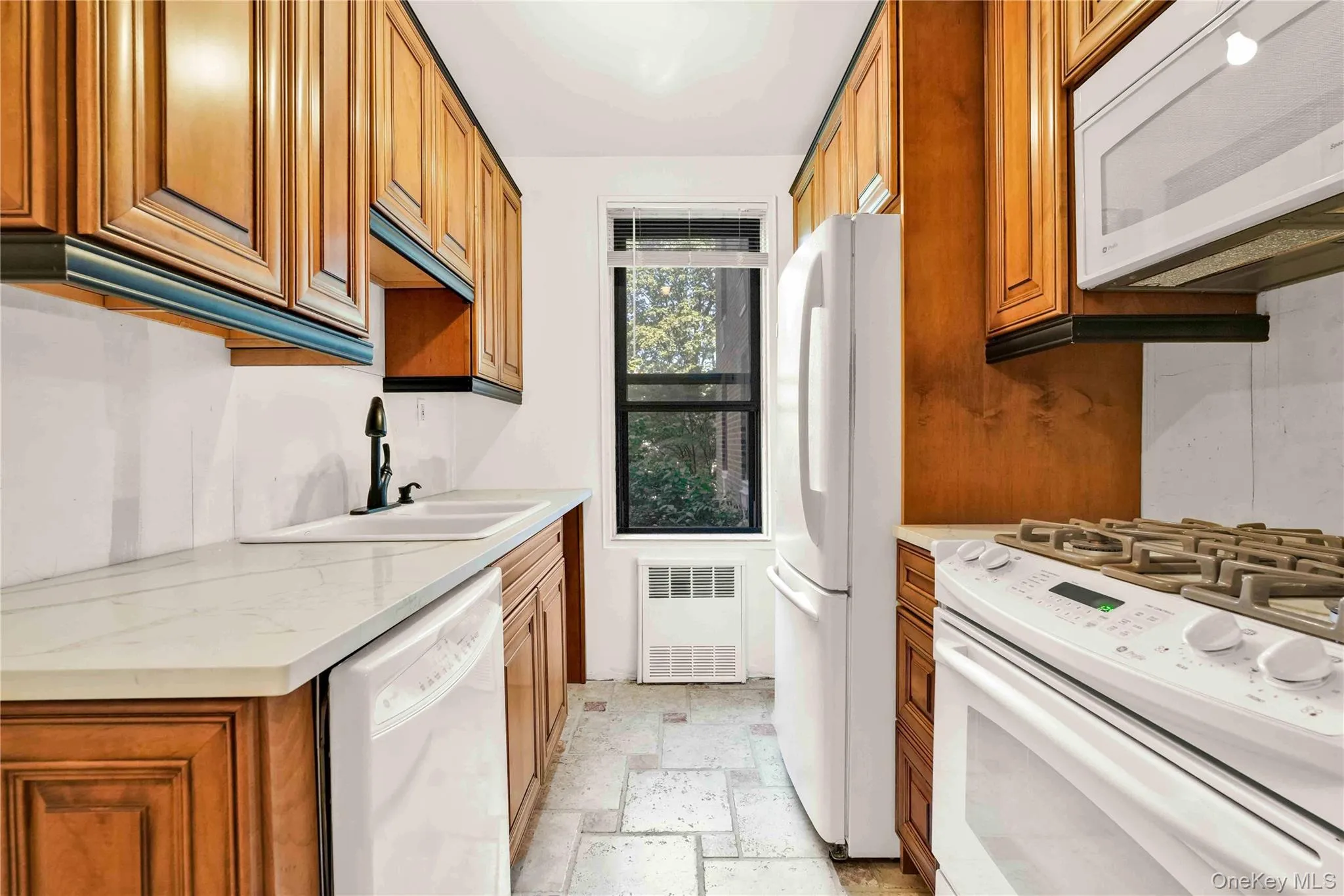 Kitchen featuring white appliances, brown cabinets, stone tile floors, light stone countertops, and radiator Kitchen featuring white appliances, brown cabinets, stone tile floors, light stone countertops, and radiator