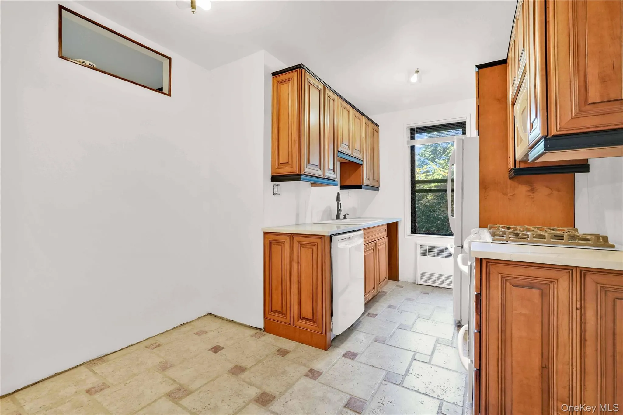 Kitchen featuring brown cabinets, stone tile flooring, dishwasher, radiator heating unit, and gas stove Kitchen featuring brown cabinets, stone tile flooring, dishwasher, radiator heating unit, and gas stove