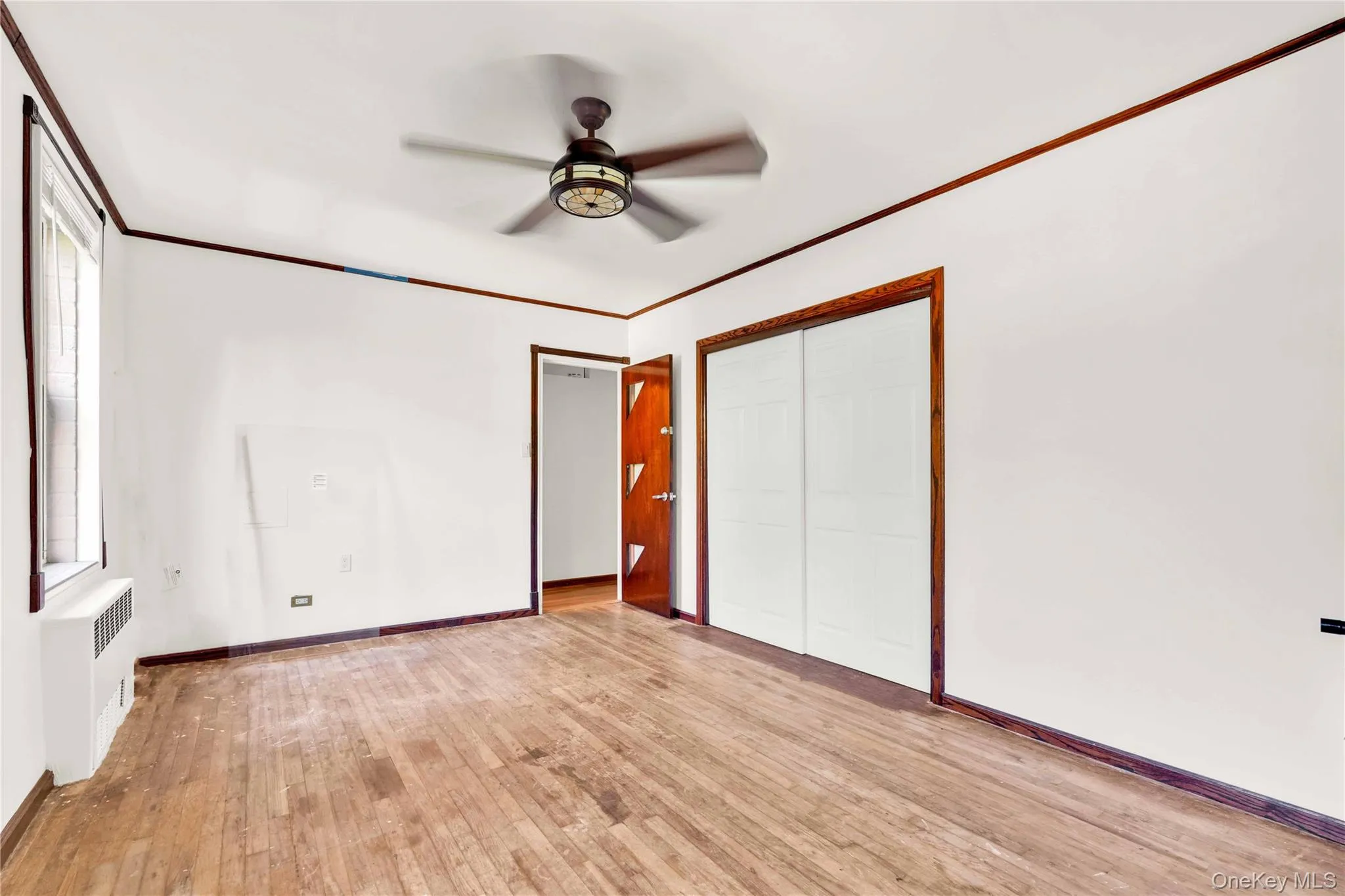 Unfurnished bedroom with ornamental molding, light wood-type flooring, radiator, a closet, and ceiling fan Unfurnished bedroom with ornamental molding, light wood-type flooring, radiator, a closet, and ceiling fan