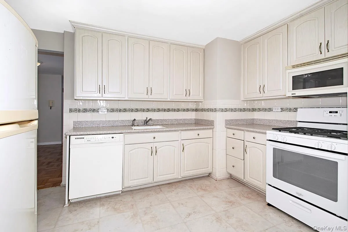 Kitchen featuring white appliances, decorative backsplash, light tile patterned floors, and cream cabinets Kitchen featuring white appliances, decorative backsplash, light tile patterned floors, and cream cabinets
