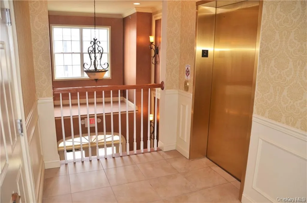 Corridor with wainscoting, elevator, wallpapered walls, a decorative wall, and light tile patterned floors Corridor with wainscoting, elevator, wallpapered walls, a decorative wall, and light tile patterned floors