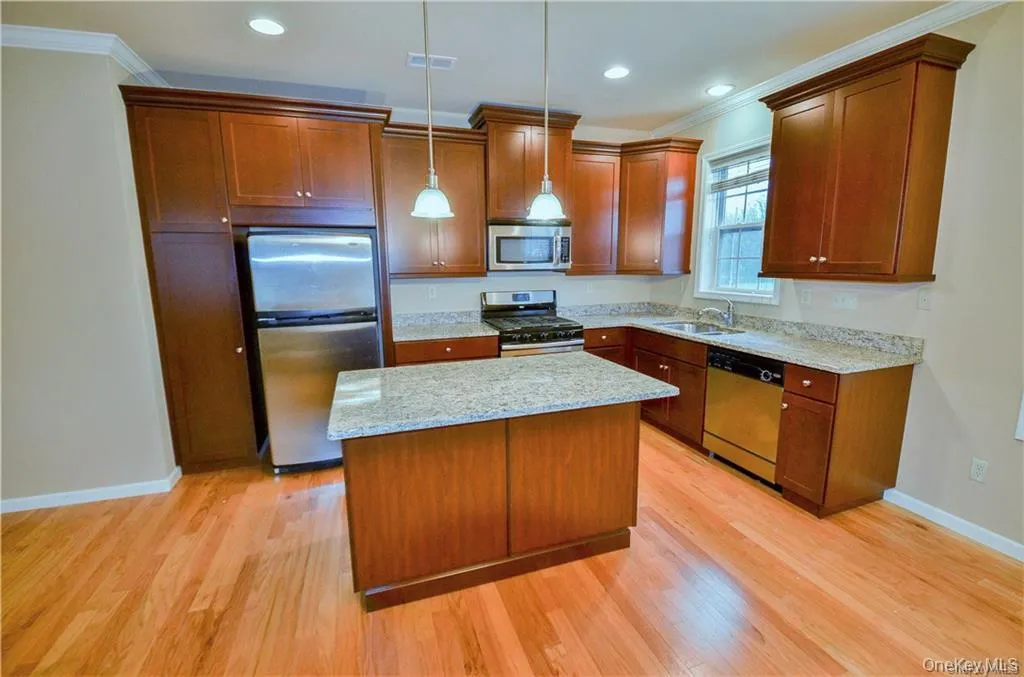 Kitchen featuring ornamental molding, appliances with stainless steel finishes, brown cabinets, light stone counters, and pendant lighting Kitchen featuring ornamental molding, appliances with stainless steel finishes, brown cabinets, light stone counters, and pendant lighting