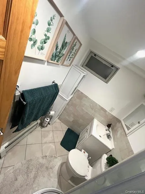 Bathroom with baseboard heating, light tile patterned flooring, and tile walls Bathroom with baseboard heating, light tile patterned flooring, and tile walls