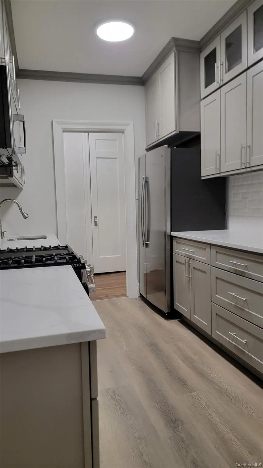 Kitchen featuring light wood-type flooring, gray cabinets, light stone counters, appliances with stainless steel finishes, and glass insert cabinets Kitchen featuring light wood-type flooring, gray cabinets, light stone counters, appliances with stainless steel finishes, and glass insert cabinets