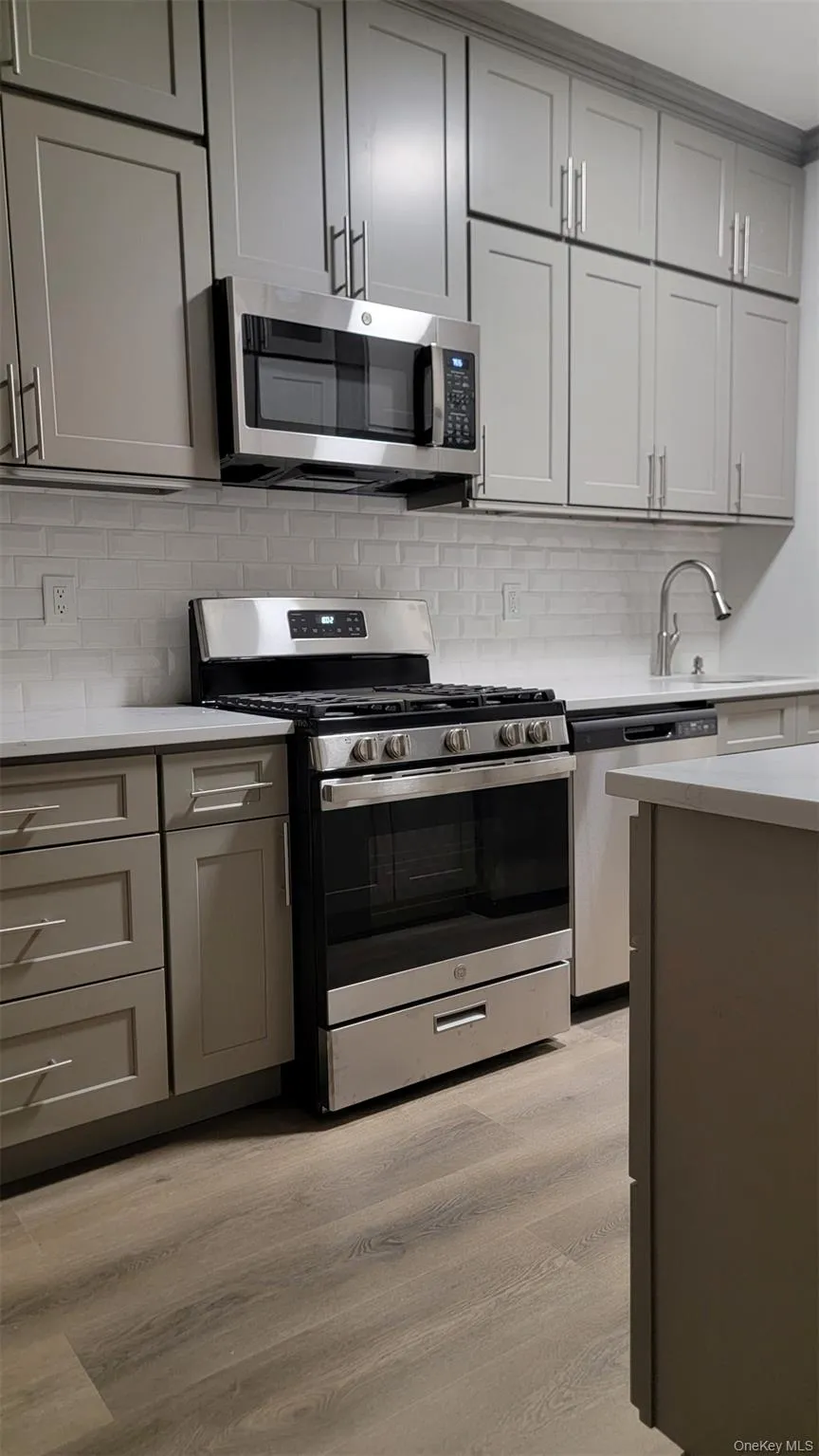Kitchen featuring gray cabinets, stainless steel appliances, light wood-style flooring, and backsplash Kitchen featuring gray cabinets, stainless steel appliances, light wood-style flooring, and backsplash