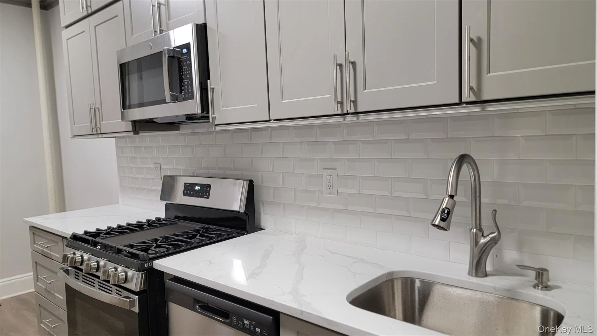 Kitchen featuring stainless steel appliances, backsplash, light stone counters, and wood finished floors Kitchen featuring stainless steel appliances, backsplash, light stone counters, and wood finished floors