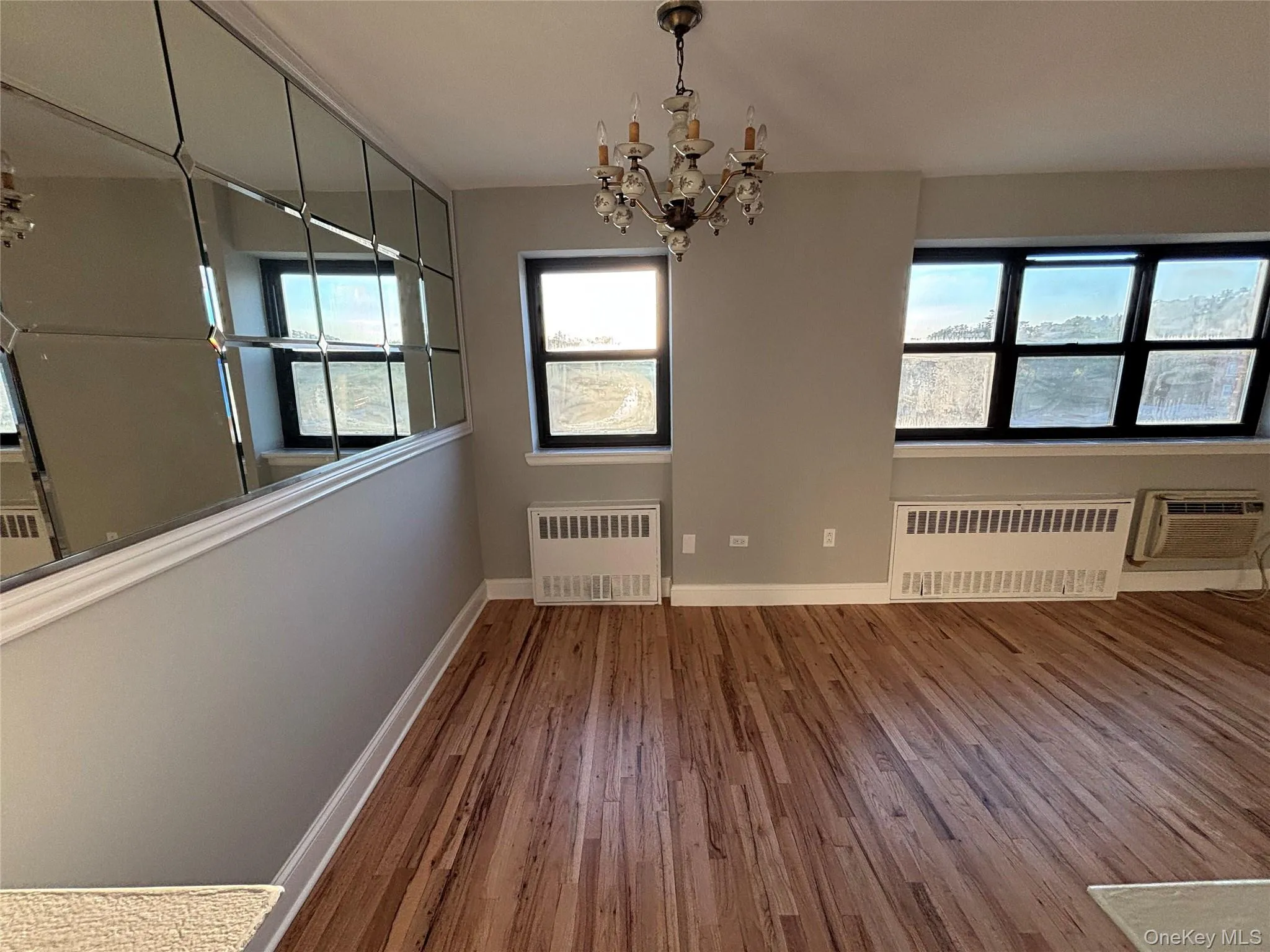 Unfurnished dining area featuring a chandelier, radiator heating unit, wood finished floors, and healthy amount of natural light Unfurnished dining area featuring a chandelier, radiator heating unit, wood finished floors, and healthy amount of natural light
