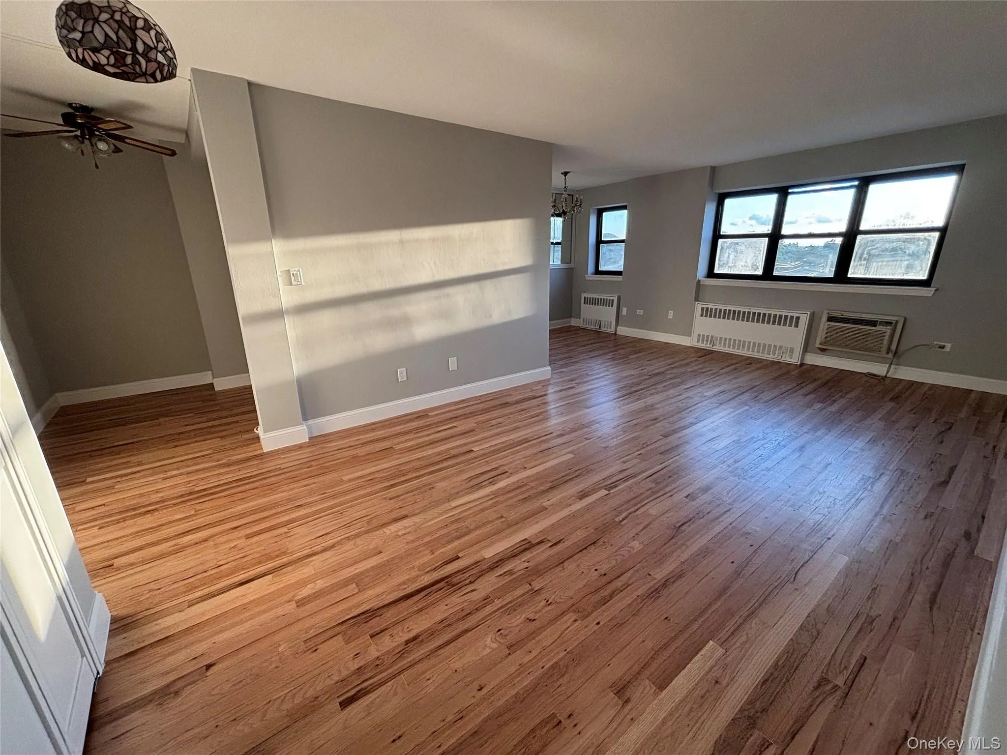 Unfurnished living room with light wood-type flooring, a chandelier, radiator heating unit, and a ceiling fan Unfurnished living room with light wood-type flooring, a chandelier, radiator heating unit, and a ceiling fan