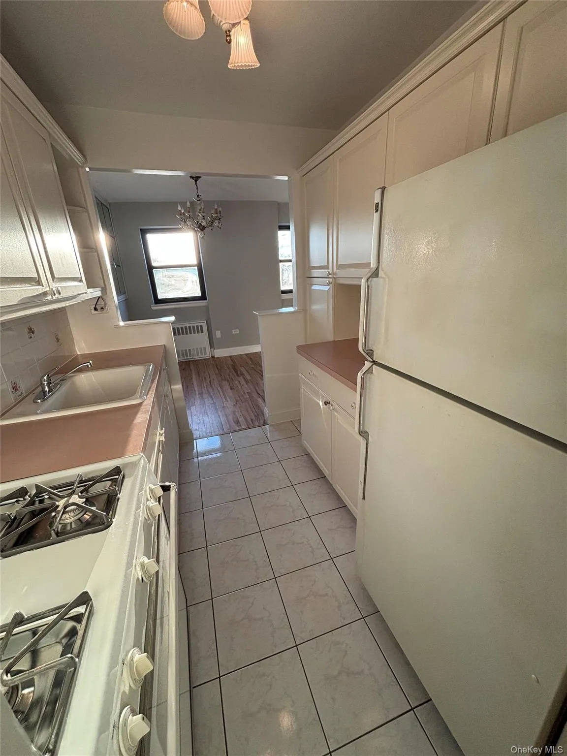Kitchen featuring white appliances, radiator heating unit, white cabinets, light countertops, and a chandelier Kitchen featuring white appliances, radiator heating unit, white cabinets, light countertops, and a chandelier