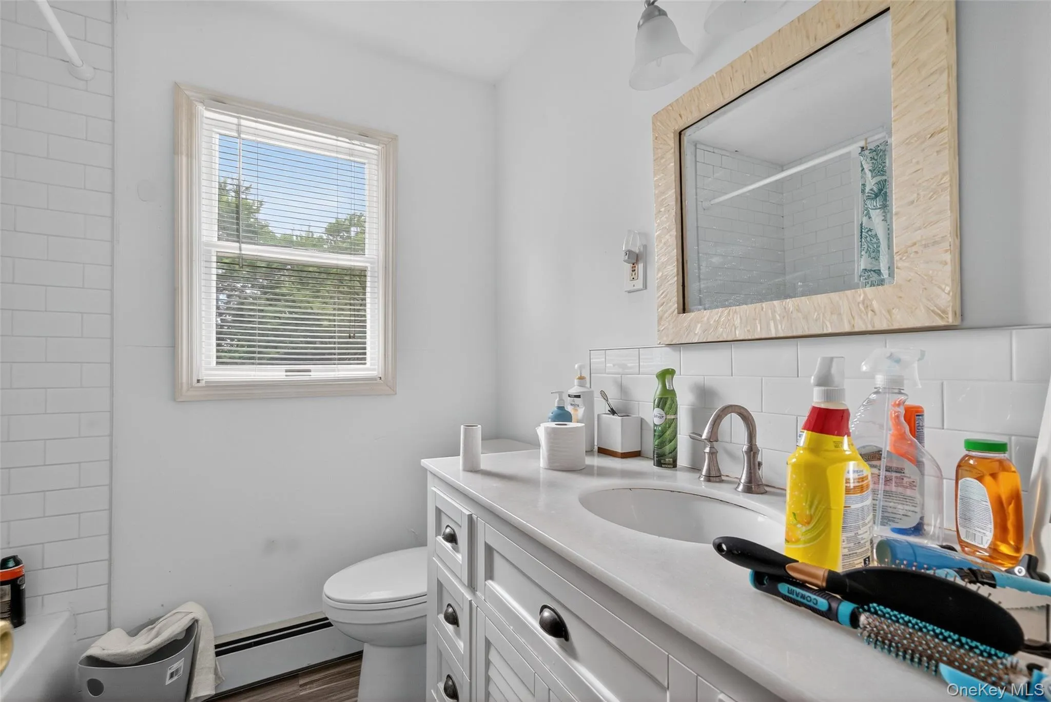 Bathroom with a baseboard heating unit, vanity, shower / bath combo with shower curtain, and tasteful backsplash Bathroom with a baseboard heating unit, vanity, shower / bath combo with shower curtain, and tasteful backsplash