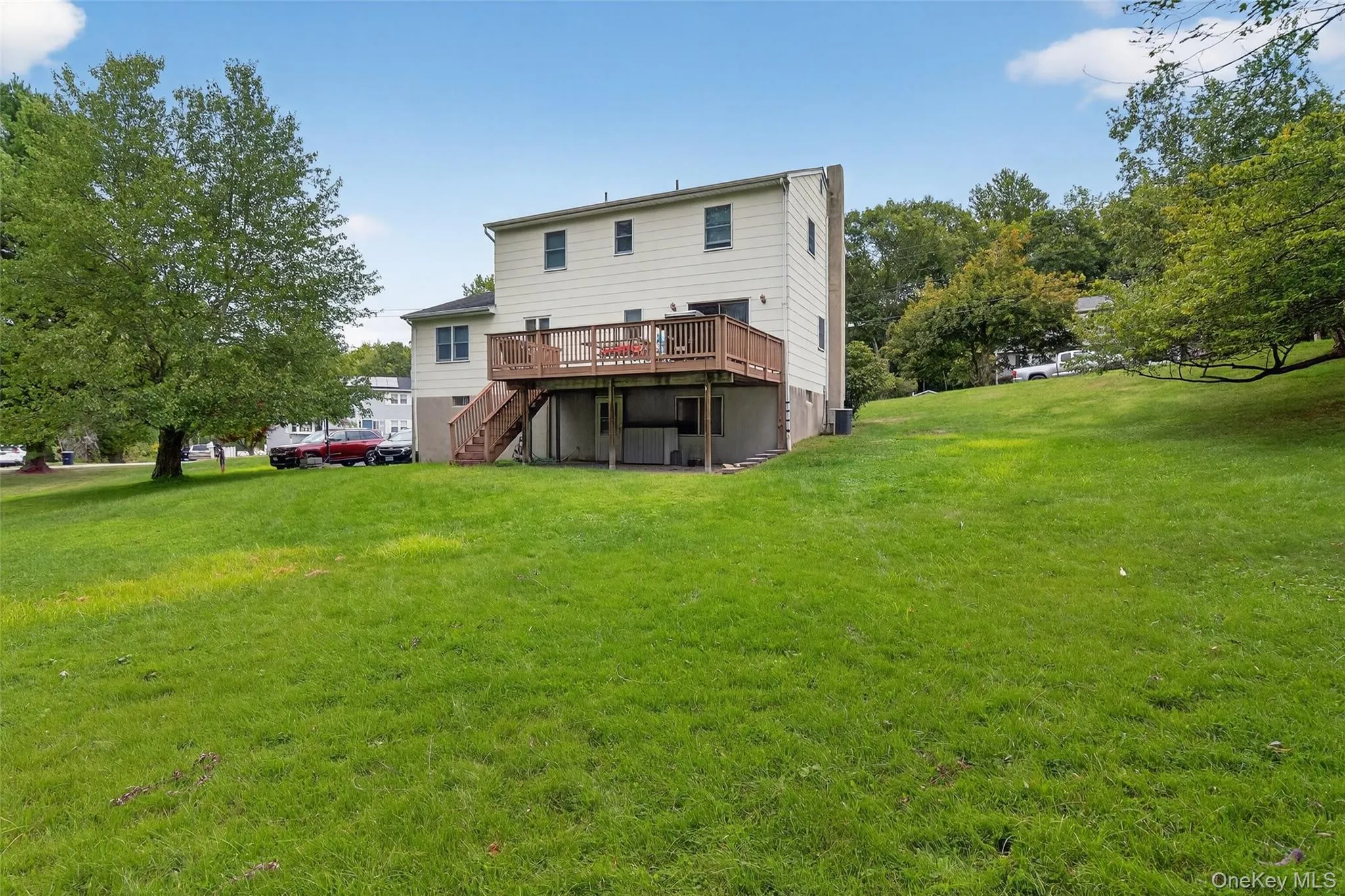 Rear view of property featuring a deck, a lawn, and stairs Rear view of property featuring a deck, a lawn, and stairs