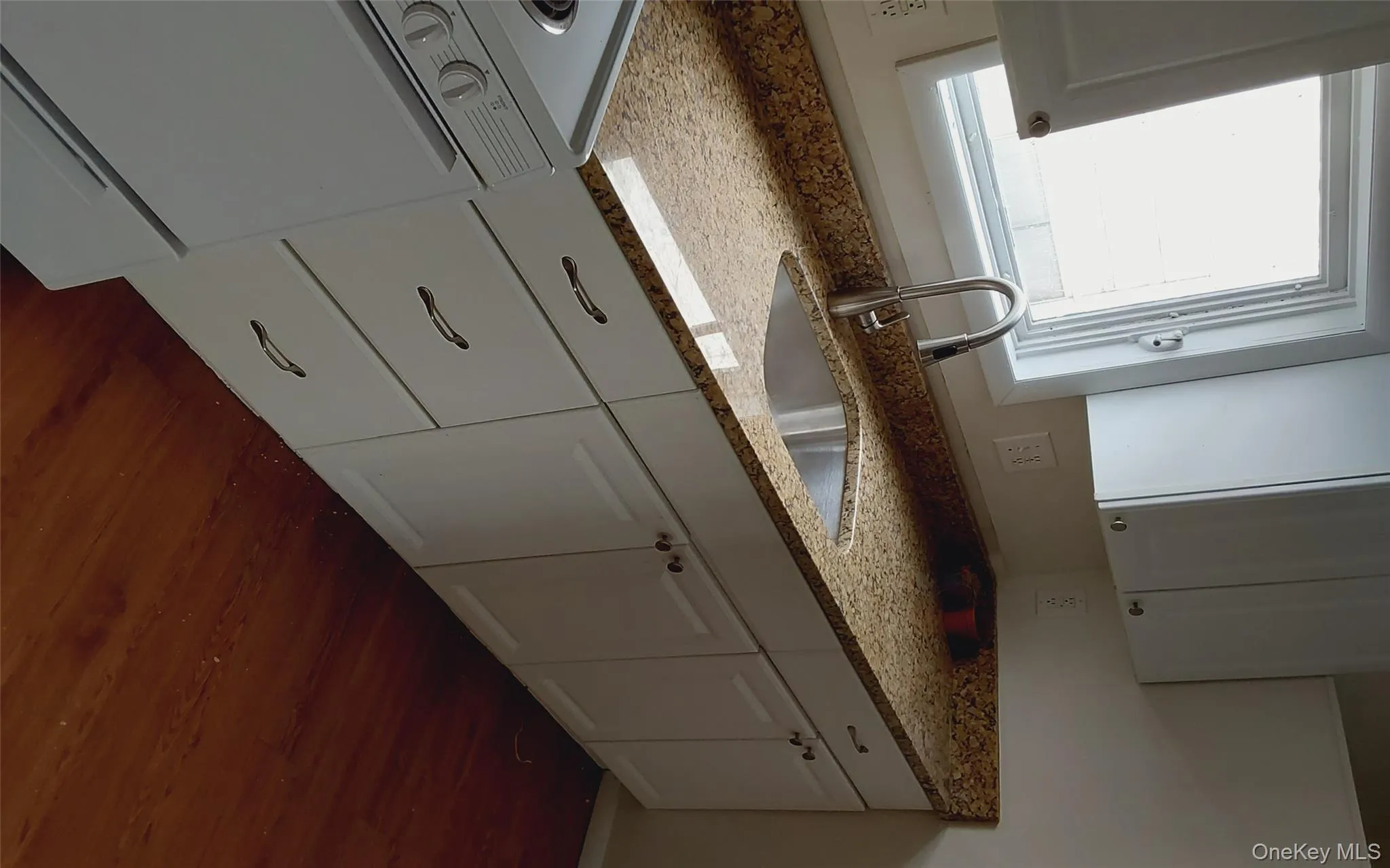 Kitchen with stove, light stone counters, white cabinets, and dark wood-style floors Kitchen with stove, light stone counters, white cabinets, and dark wood-style floors