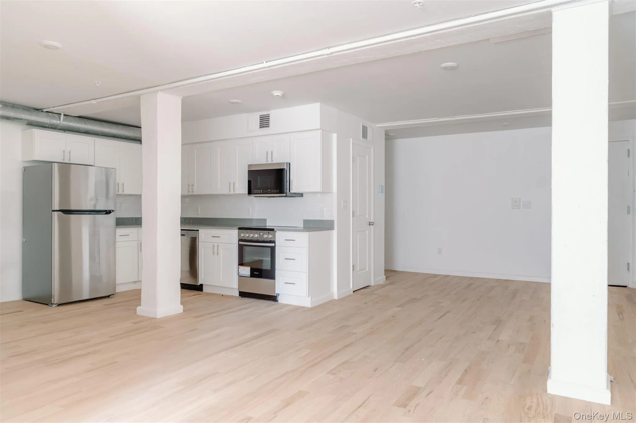 Kitchen featuring stainless steel appliances, decorative backsplash, white cabinetry, light wood finished floors, and light countertops Kitchen featuring stainless steel appliances, decorative backsplash, white cabinetry, light wood finished floors, and light countertops