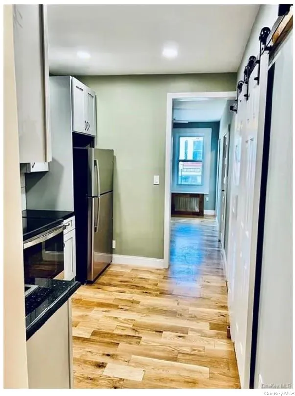 Kitchen with a barn door, light wood-type flooring, white cabinetry, and stainless steel appliances Kitchen with a barn door, light wood-type flooring, white cabinetry, and stainless steel appliances
