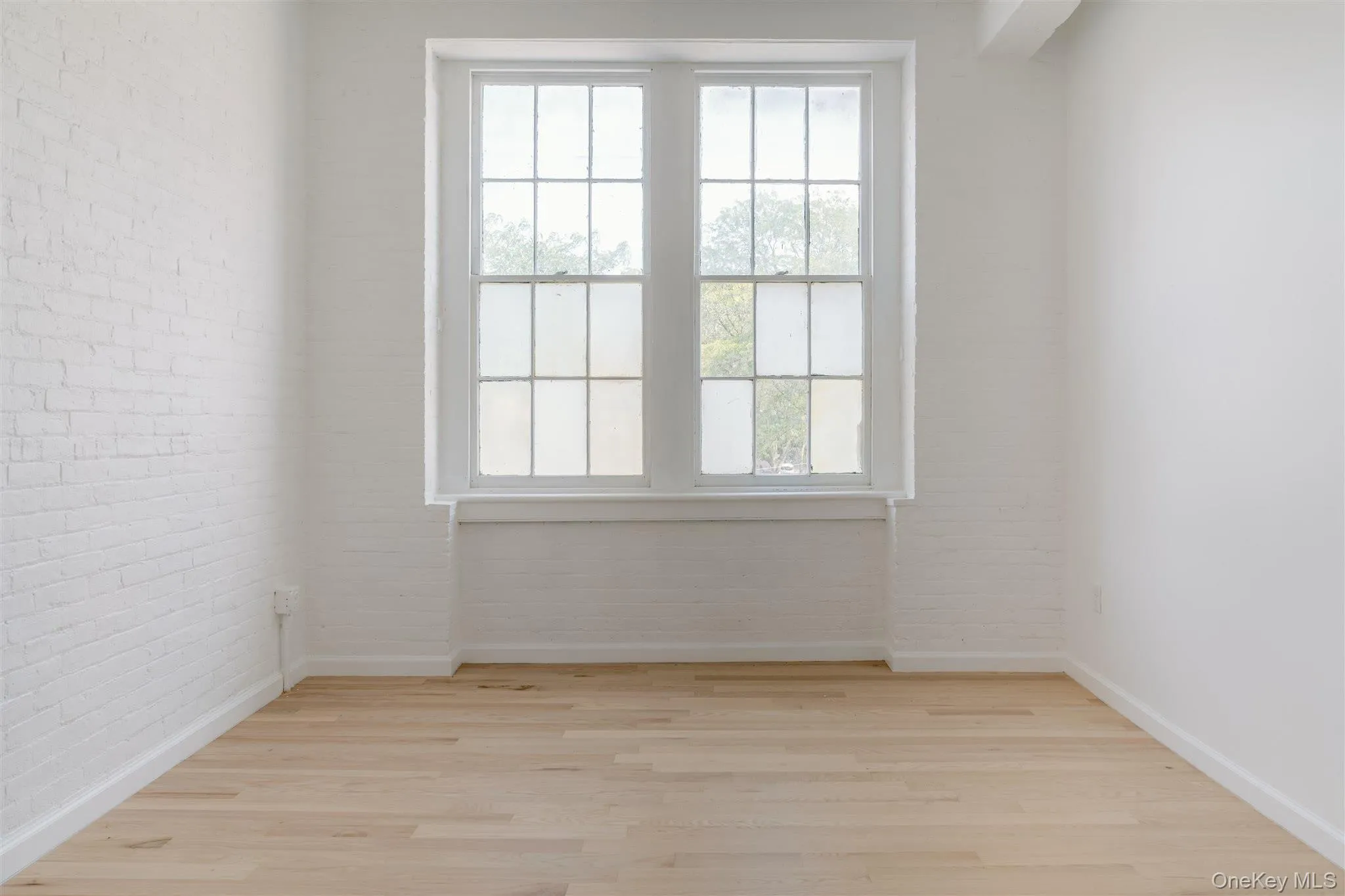 Empty room featuring light wood-style floors and brick wall Empty room featuring light wood-style floors and brick wall