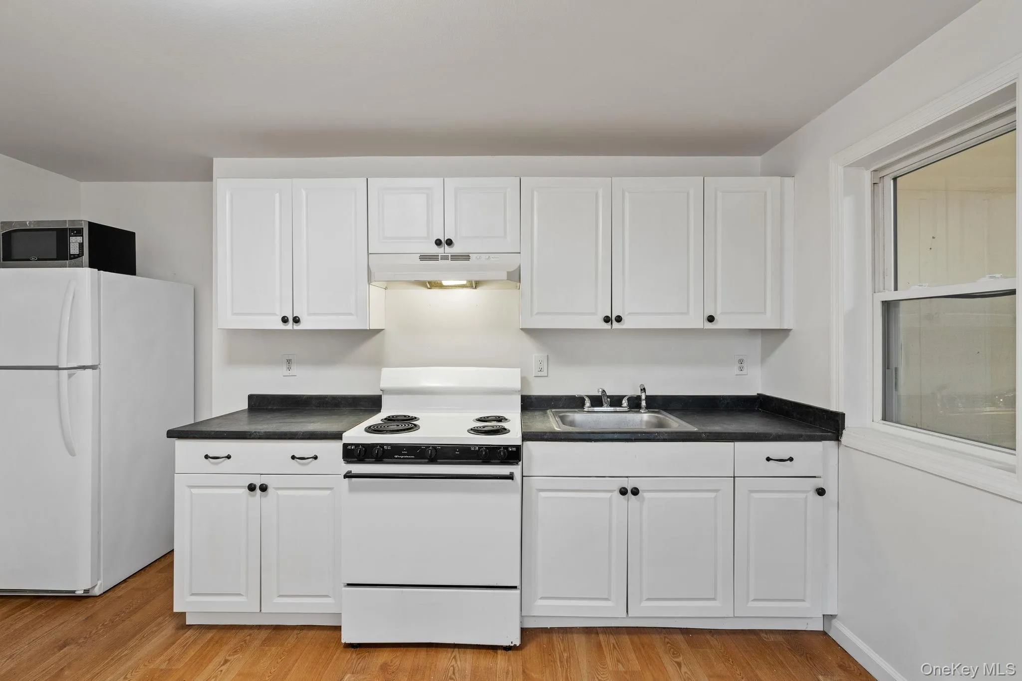 Kitchen featuring white appliances, dark countertops, white cabinetry, and light wood-style floors Kitchen featuring white appliances, dark countertops, white cabinetry, and light wood-style floors