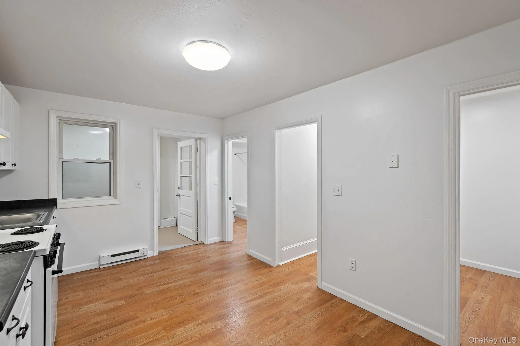 Kitchen with white electric range oven, dark countertops, white cabinets, light wood-style floors, and a baseboard heating unit Kitchen with white electric range oven, dark countertops, white cabinets, light wood-style floors, and a baseboard heating unit