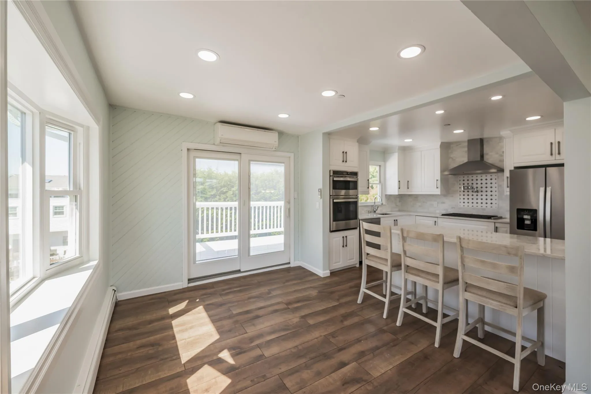 Kitchen featuring white cabinetry, a breakfast bar area, stainless steel appliances, light stone counters, and dark wood-style floors Kitchen featuring white cabinetry, a breakfast bar area, stainless steel appliances, light stone counters, and dark wood-style floors
