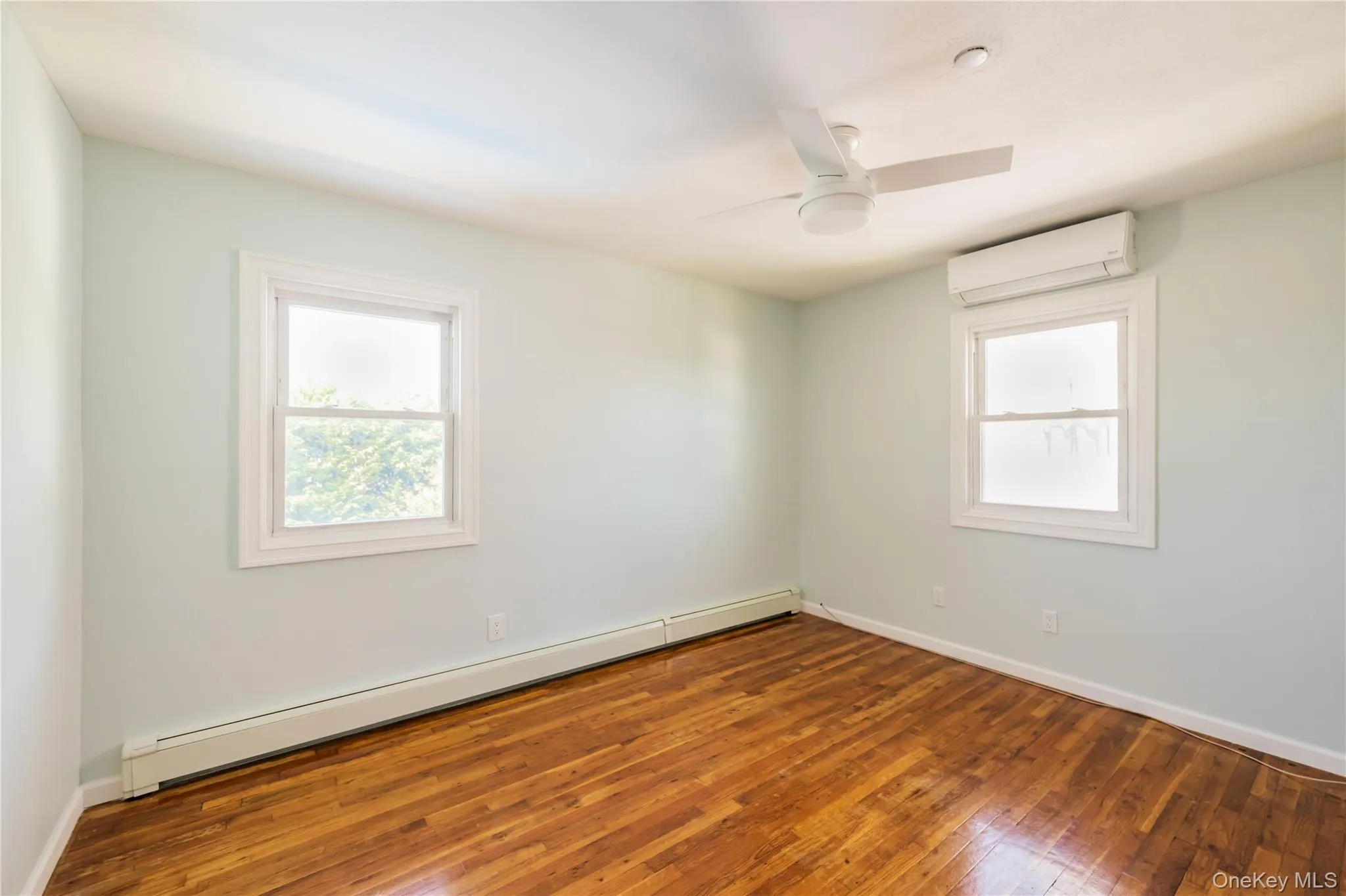Spare room with a baseboard heating unit, hardwood / wood-style flooring, an AC wall unit, and a ceiling fan Spare room with a baseboard heating unit, hardwood / wood-style flooring, an AC wall unit, and a ceiling fan
