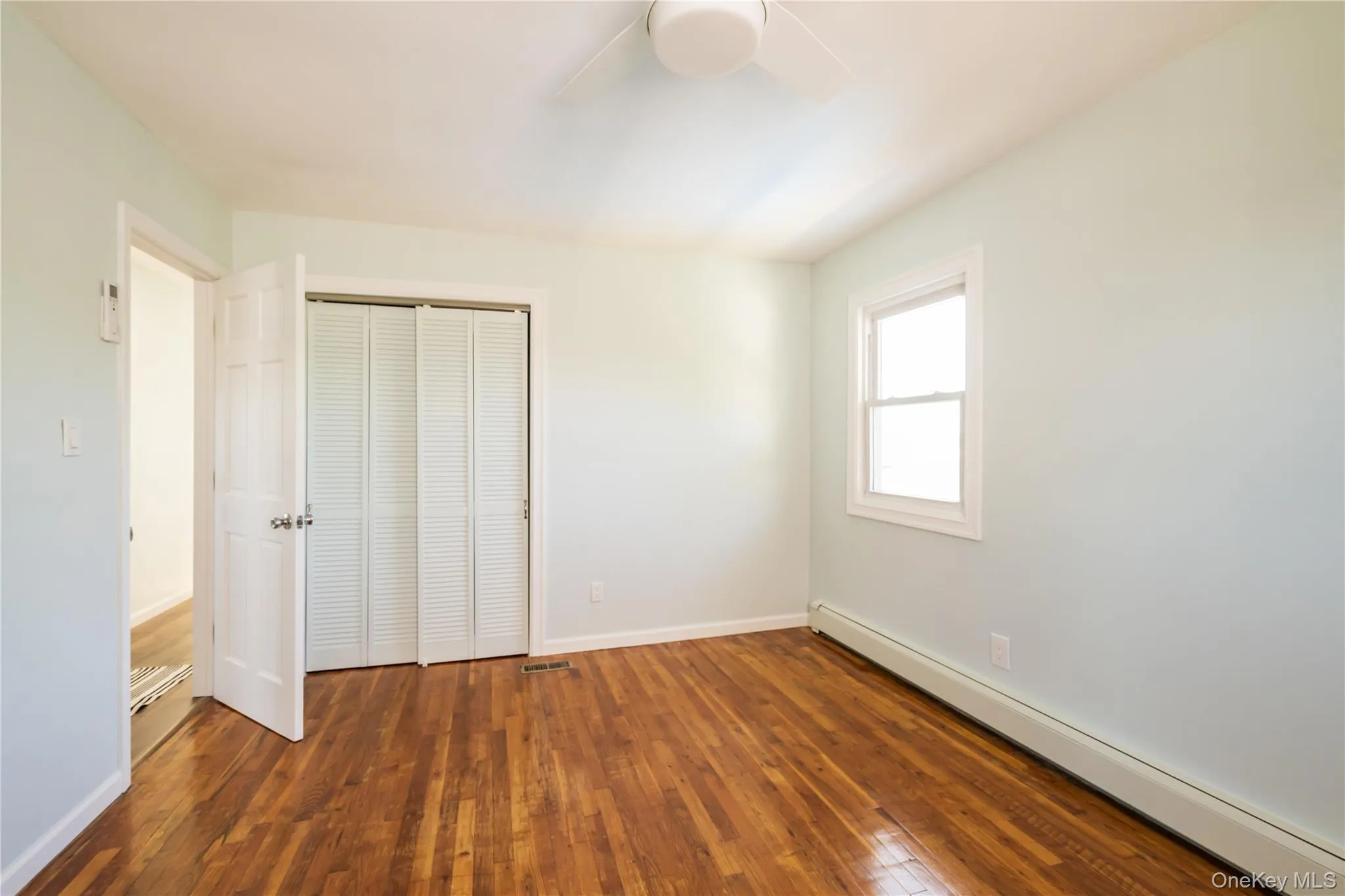 Unfurnished bedroom featuring a baseboard heating unit, dark wood finished floors, a closet, and a ceiling fan Unfurnished bedroom featuring a baseboard heating unit, dark wood finished floors, a closet, and a ceiling fan