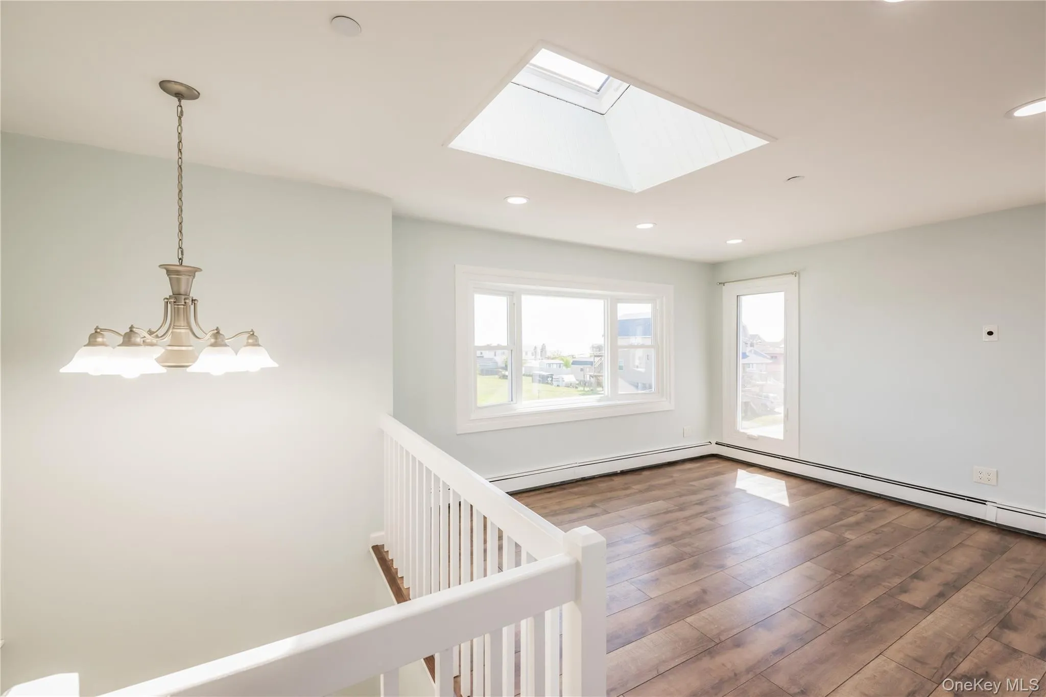 Unfurnished room featuring a skylight, recessed lighting, wood finished floors, and baseboard heating Unfurnished room featuring a skylight, recessed lighting, wood finished floors, and baseboard heating