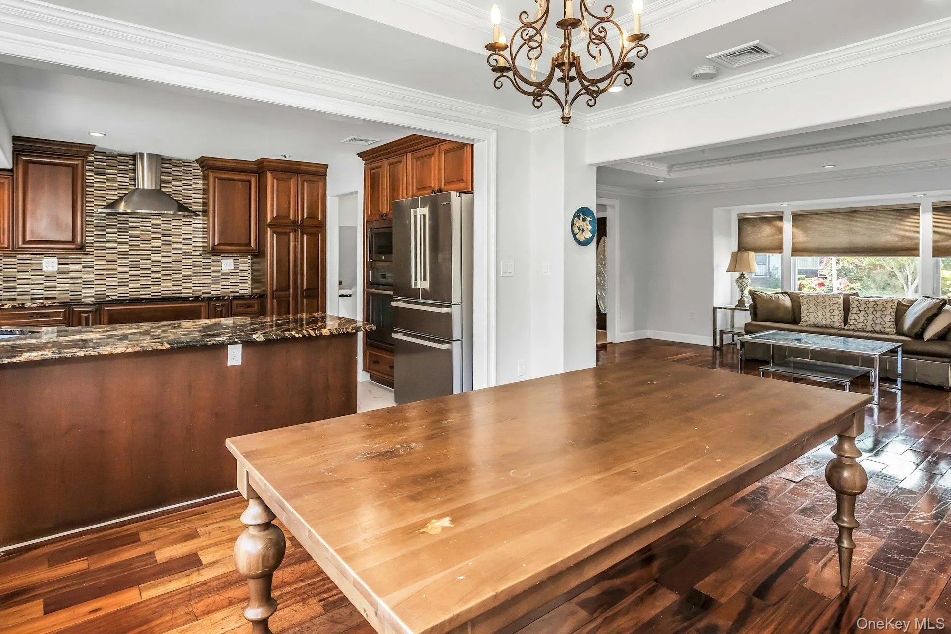 Kitchen with hanging light fixtures, dark stone counters, ornamental molding, backsplash, and wall chimney range hood Kitchen with hanging light fixtures, dark stone counters, ornamental molding, backsplash, and wall chimney range hood