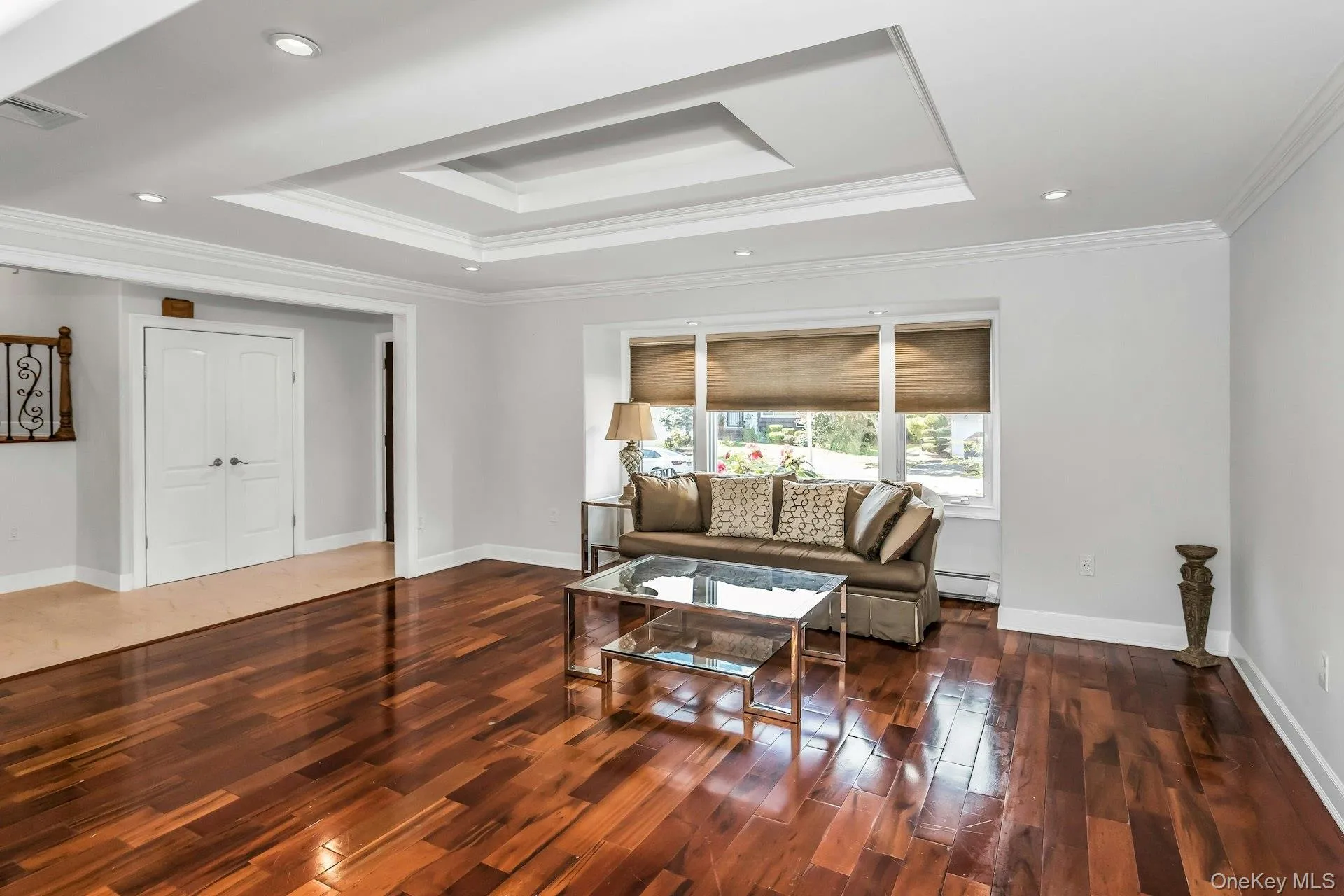 Living area featuring a tray ceiling, ornamental molding, dark wood-style flooring, recessed lighting, and baseboard heating Living area featuring a tray ceiling, ornamental molding, dark wood-style flooring, recessed lighting, and baseboard heating