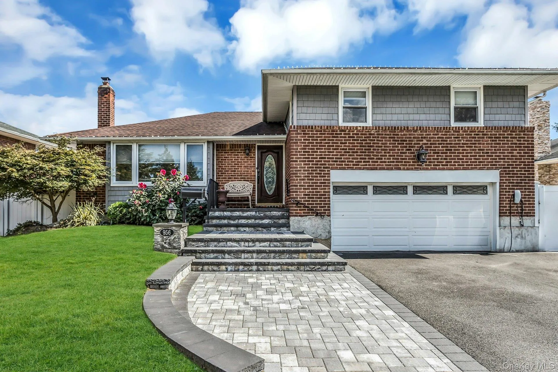 Split level home featuring asphalt driveway, a garage, a chimney, and brick siding Split level home featuring asphalt driveway, a garage, a chimney, and brick siding