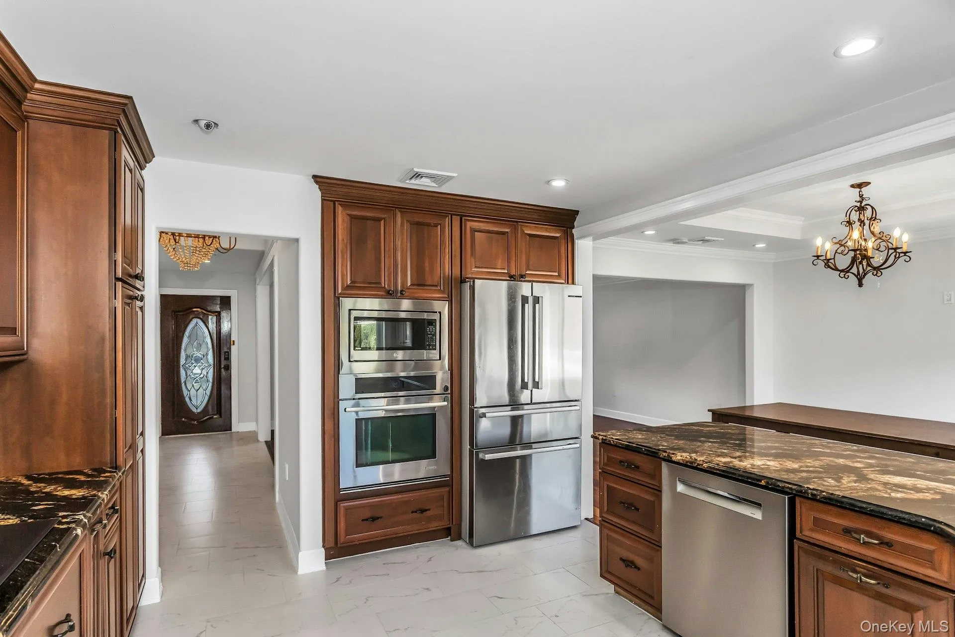Kitchen with a chandelier, dark stone counters, appliances with stainless steel finishes, light marble finish floors, and pendant lighting Kitchen with a chandelier, dark stone counters, appliances with stainless steel finishes, light marble finish floors, and pendant lighting