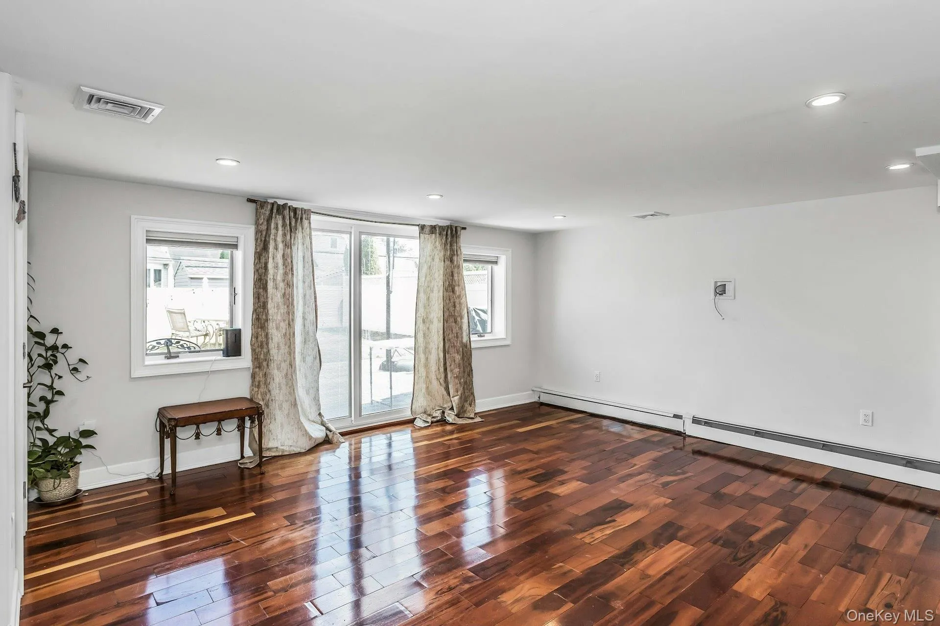 Empty room featuring dark wood finished floors, recessed lighting, and baseboard heating Empty room featuring dark wood finished floors, recessed lighting, and baseboard heating