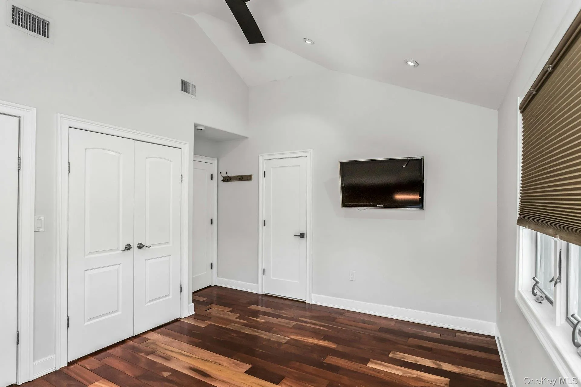 Unfurnished bedroom with dark wood-style flooring, high vaulted ceiling, and a ceiling fan Unfurnished bedroom with dark wood-style flooring, high vaulted ceiling, and a ceiling fan