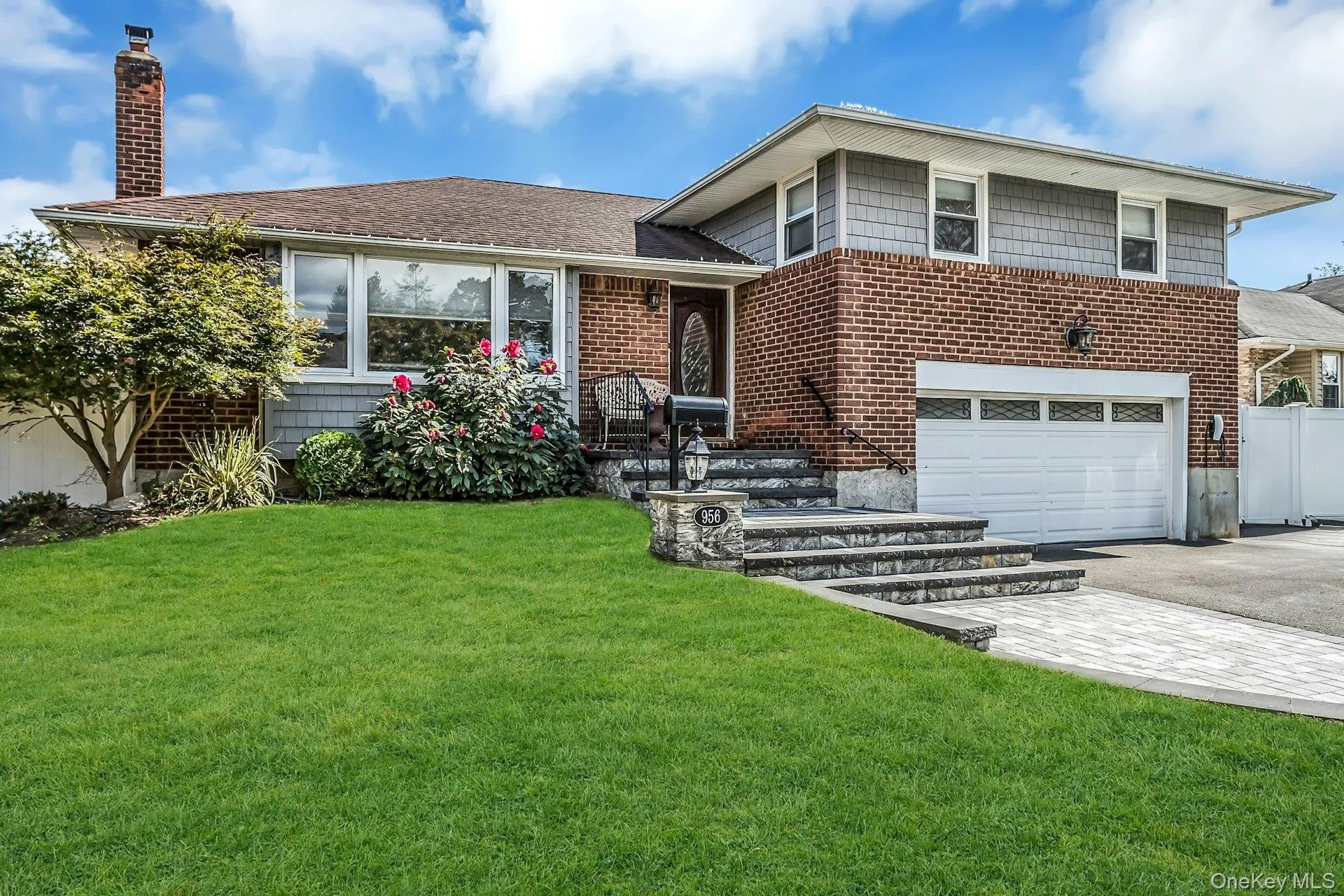 Tri-level home featuring asphalt driveway, a chimney, a garage, a front yard, and brick siding Tri-level home featuring asphalt driveway, a chimney, a garage, a front yard, and brick siding