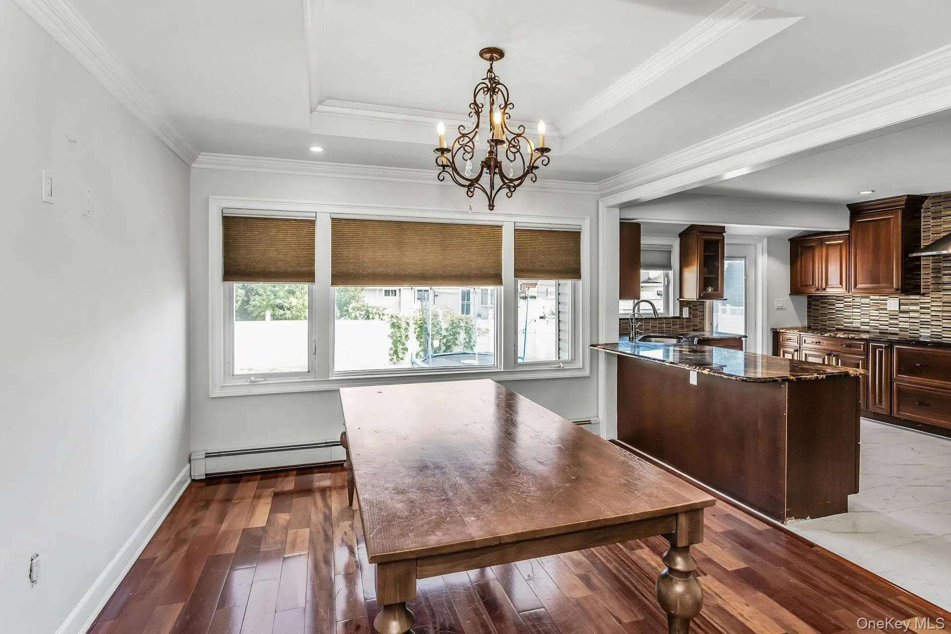 Dining space featuring a raised ceiling, a baseboard radiator, crown molding, a chandelier, and dark wood finished floors Dining space featuring a raised ceiling, a baseboard radiator, crown molding, a chandelier, and dark wood finished floors