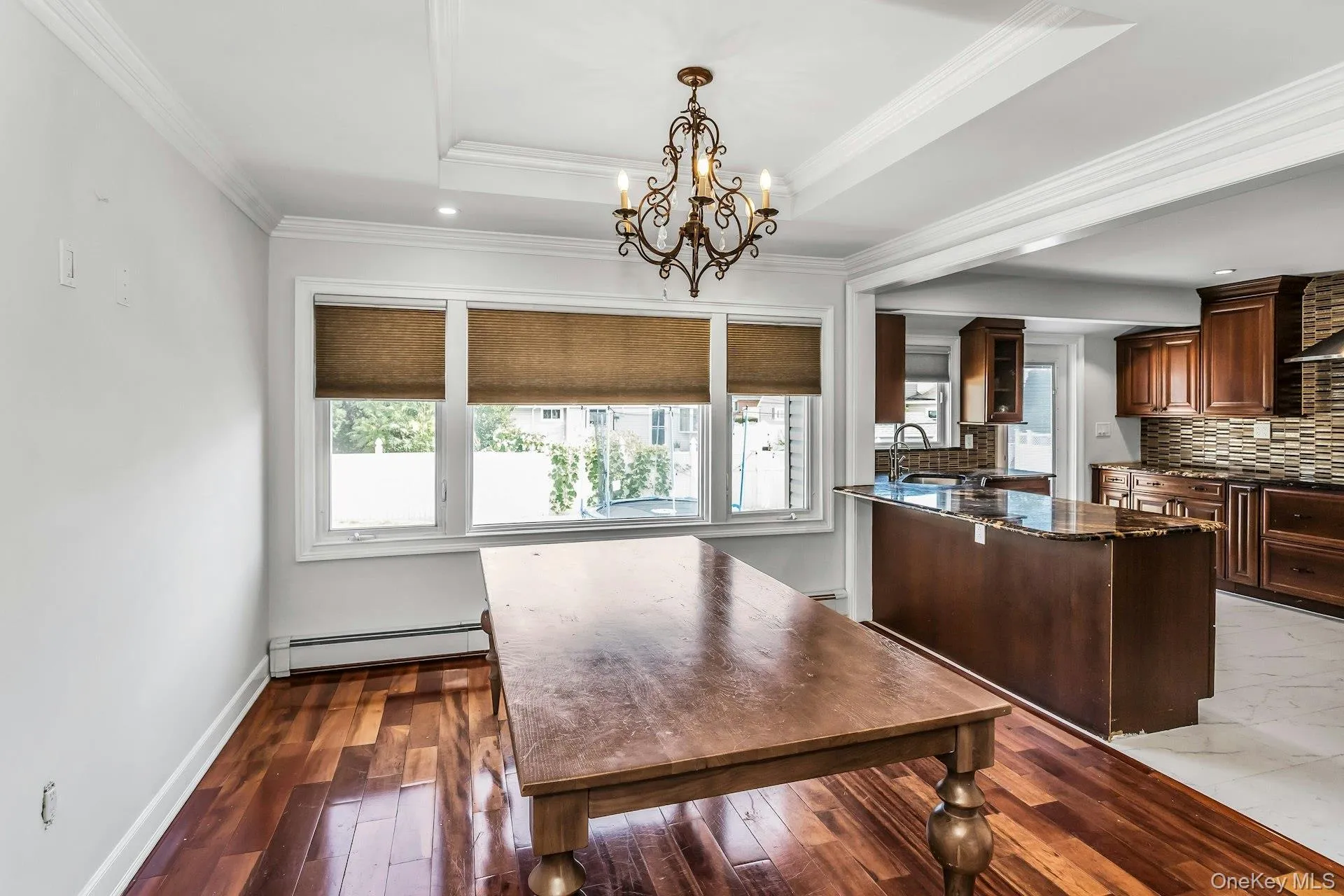 Dining room featuring a raised ceiling, a baseboard radiator, crown molding, a chandelier, and dark wood finished floors Dining room featuring a raised ceiling, a baseboard radiator, crown molding, a chandelier, and dark wood finished floors