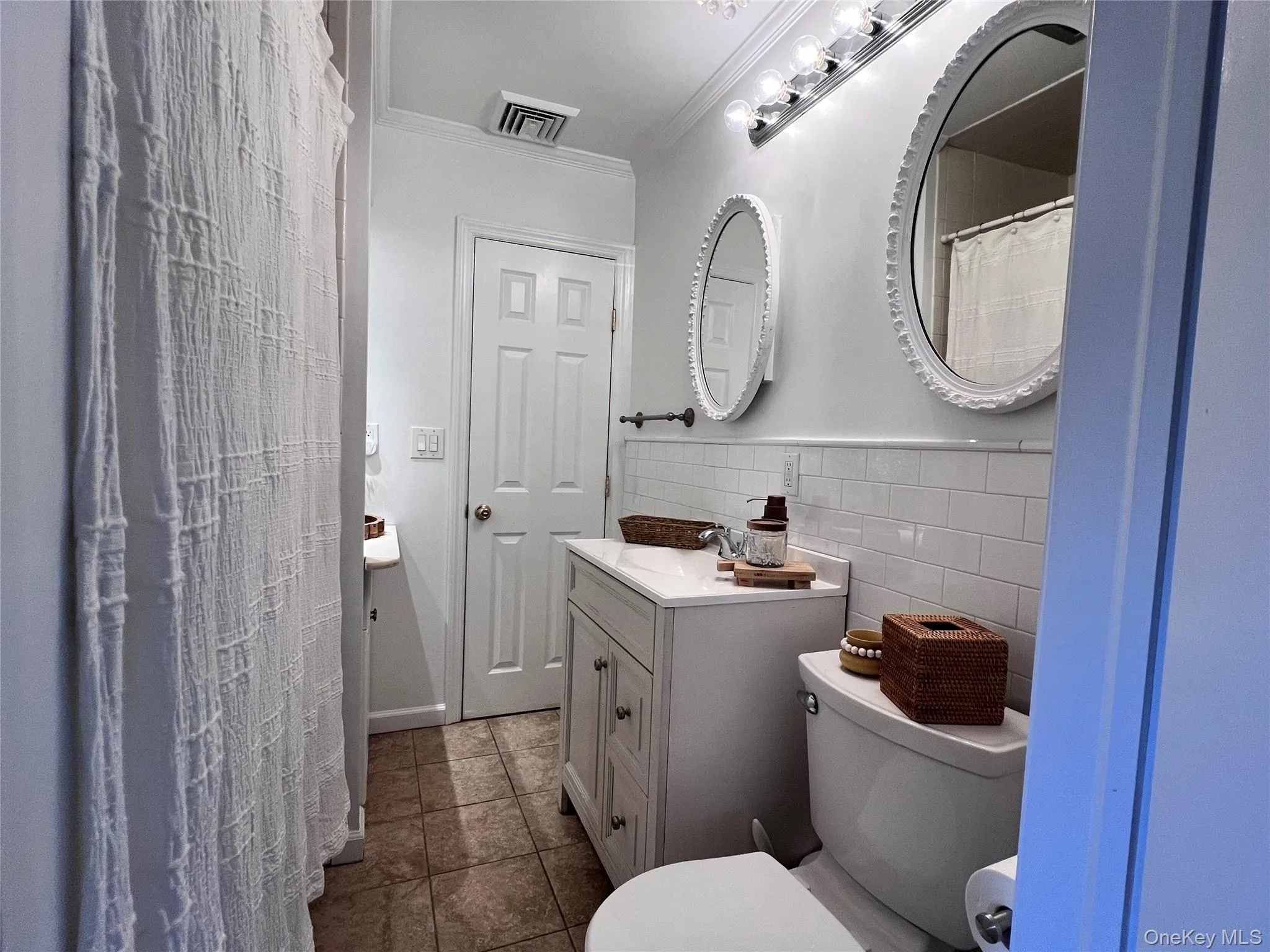 Bathroom featuring toilet, tile walls, vanity, visible vents, and crown molding Bathroom featuring toilet, tile walls, vanity, visible vents, and crown molding