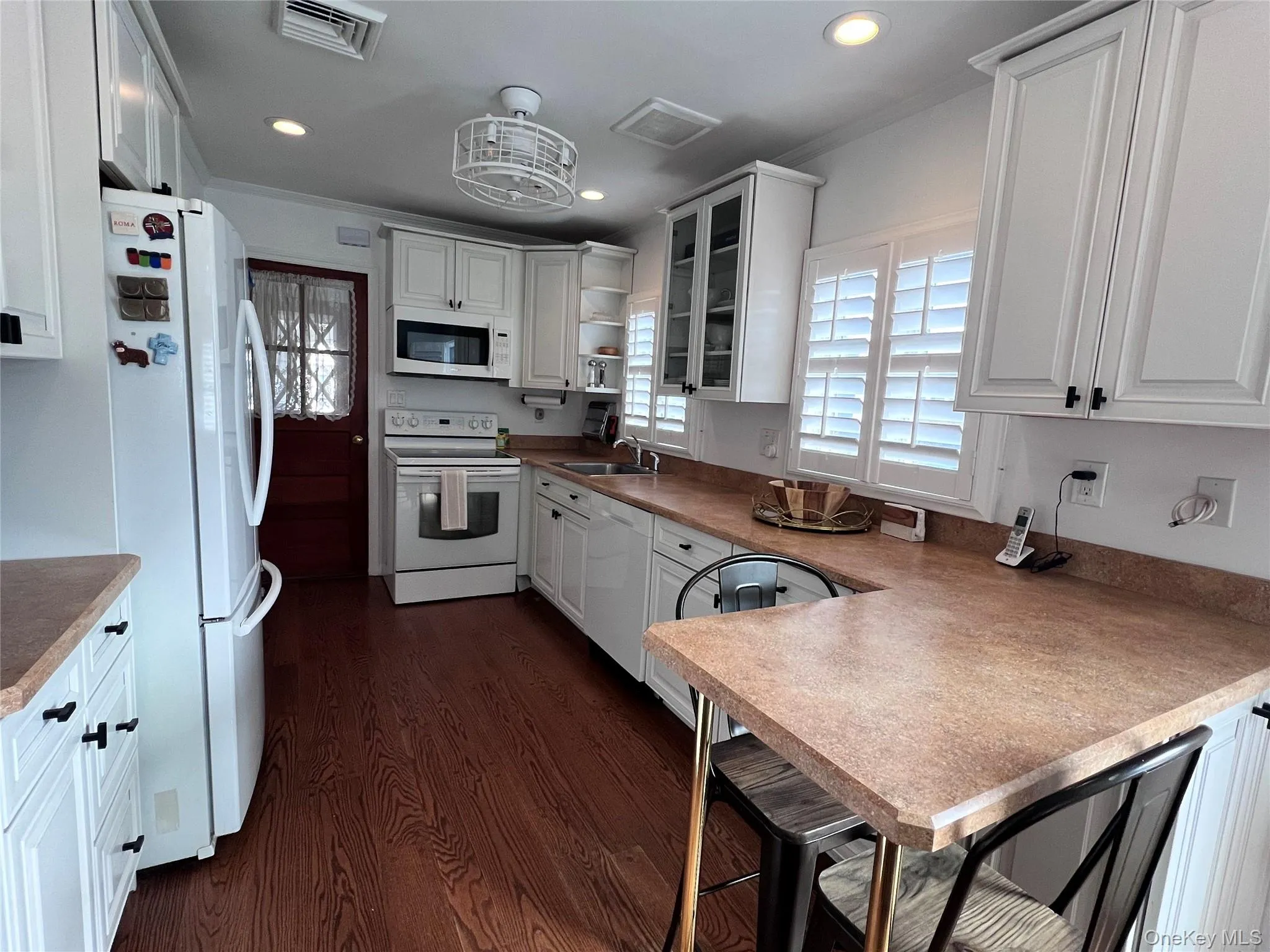 Kitchen with white appliances, a sink, visible vents, white cabinetry, and dark wood finished floors Kitchen with white appliances, a sink, visible vents, white cabinetry, and dark wood finished floors
