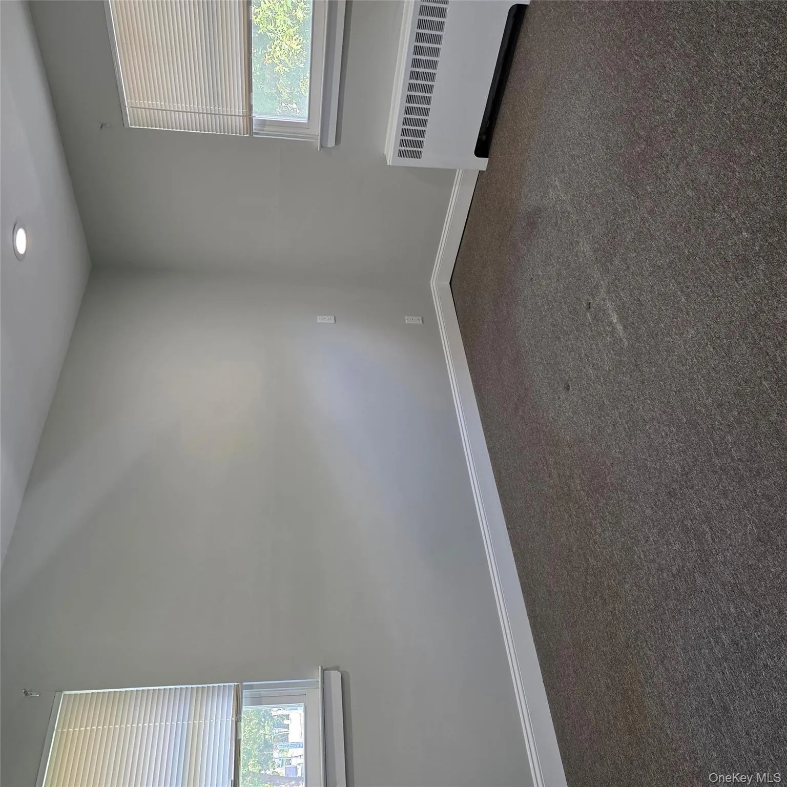 Empty room with healthy amount of natural light, radiator, dark colored carpet, and recessed lighting Empty room with healthy amount of natural light, radiator, dark colored carpet, and recessed lighting