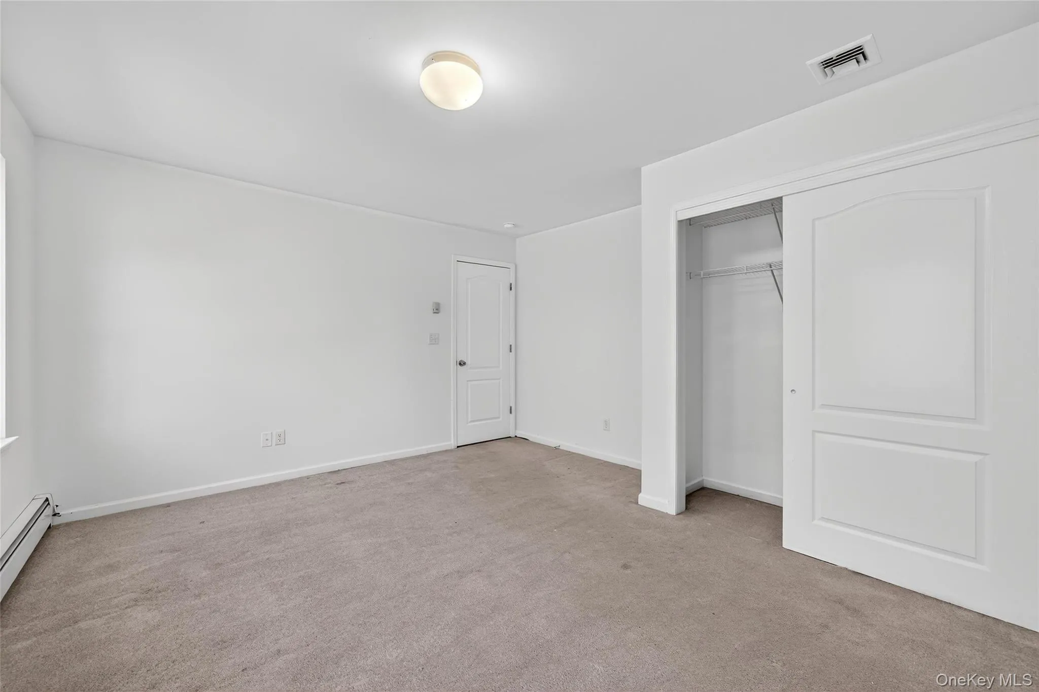 Unfurnished bedroom with light carpet, a closet, and baseboard heating Unfurnished bedroom with light carpet, a closet, and baseboard heating