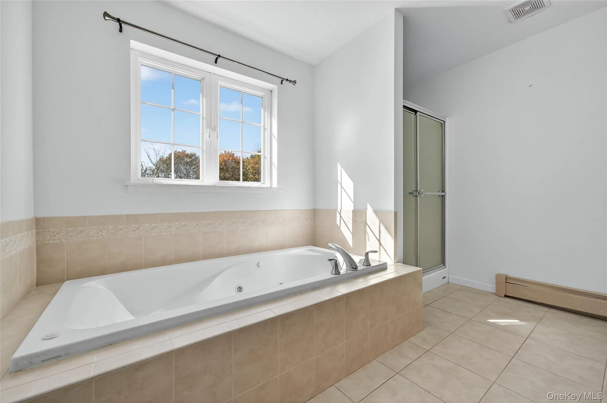 Bathroom featuring a baseboard radiator, a jetted tub, light tile patterned floors, and a stall shower Bathroom featuring a baseboard radiator, a jetted tub, light tile patterned floors, and a stall shower