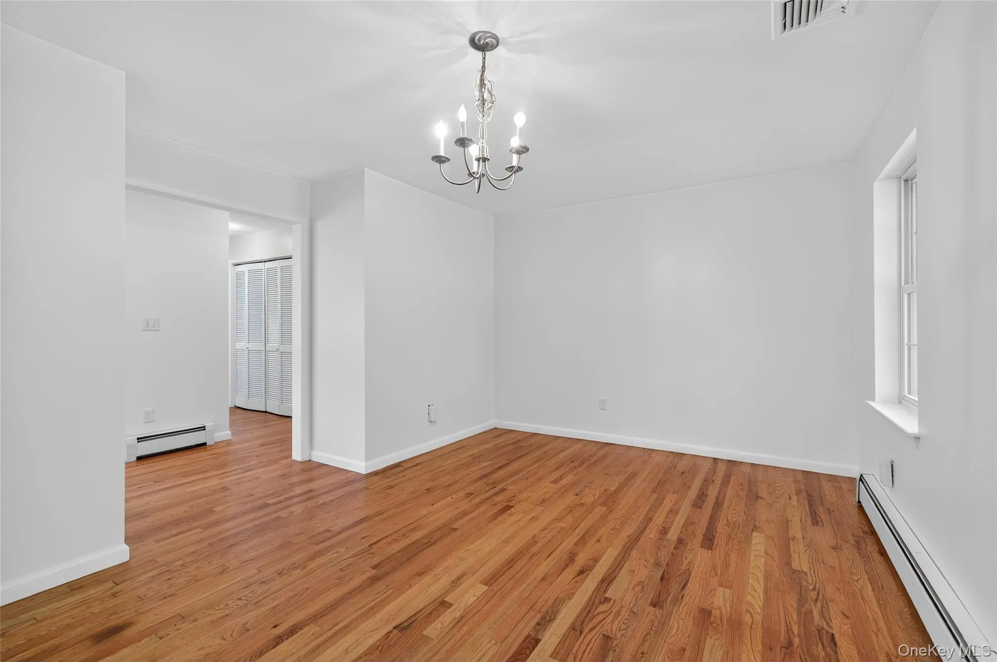 Spare room with baseboard heating, light wood-style floors, and a chandelier Spare room with baseboard heating, light wood-style floors, and a chandelier