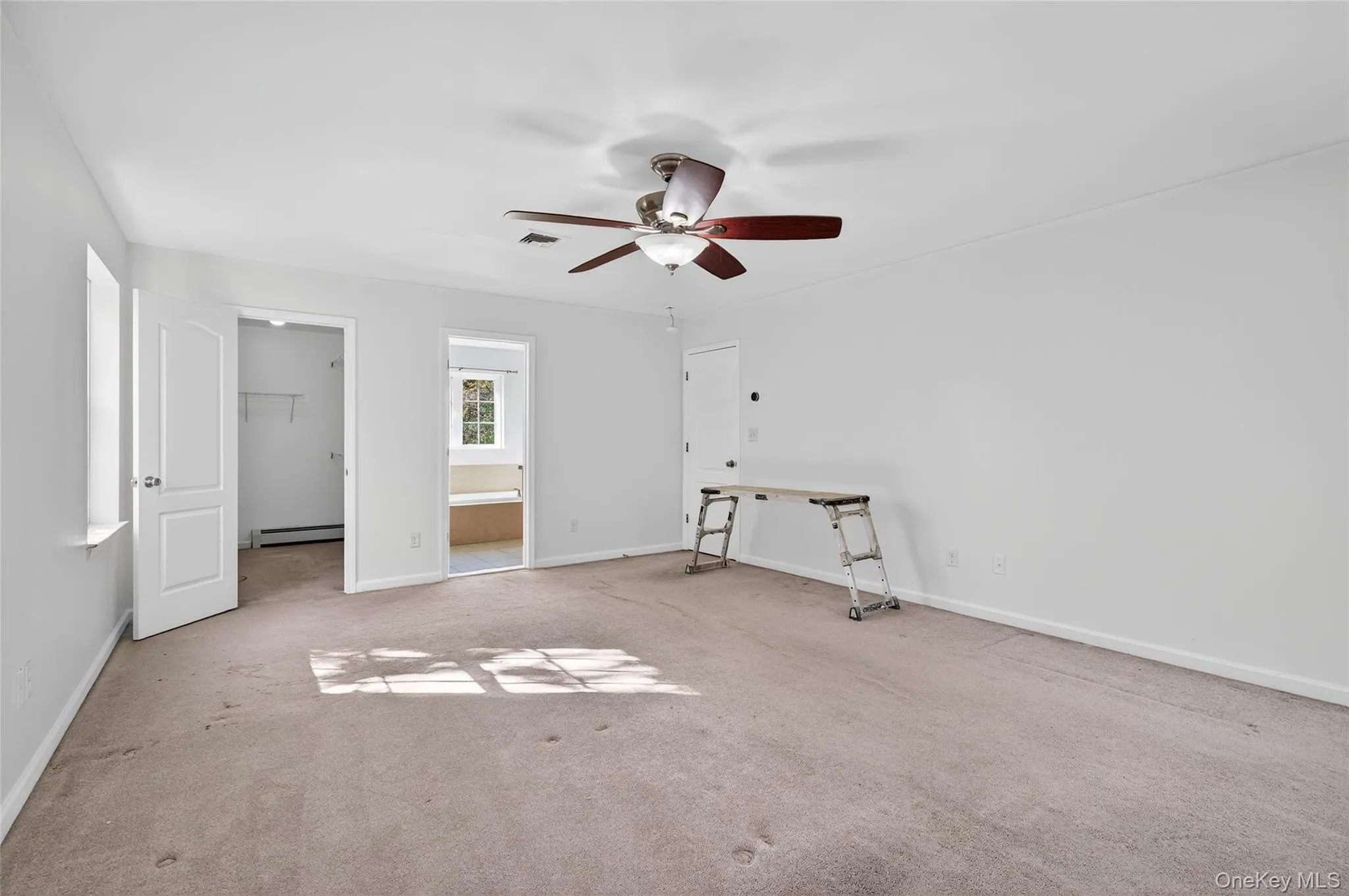 Unfurnished bedroom with a spacious closet, carpet flooring, ensuite bathroom, ceiling fan, and baseboard heating Unfurnished bedroom with a spacious closet, carpet flooring, ensuite bathroom, ceiling fan, and baseboard heating