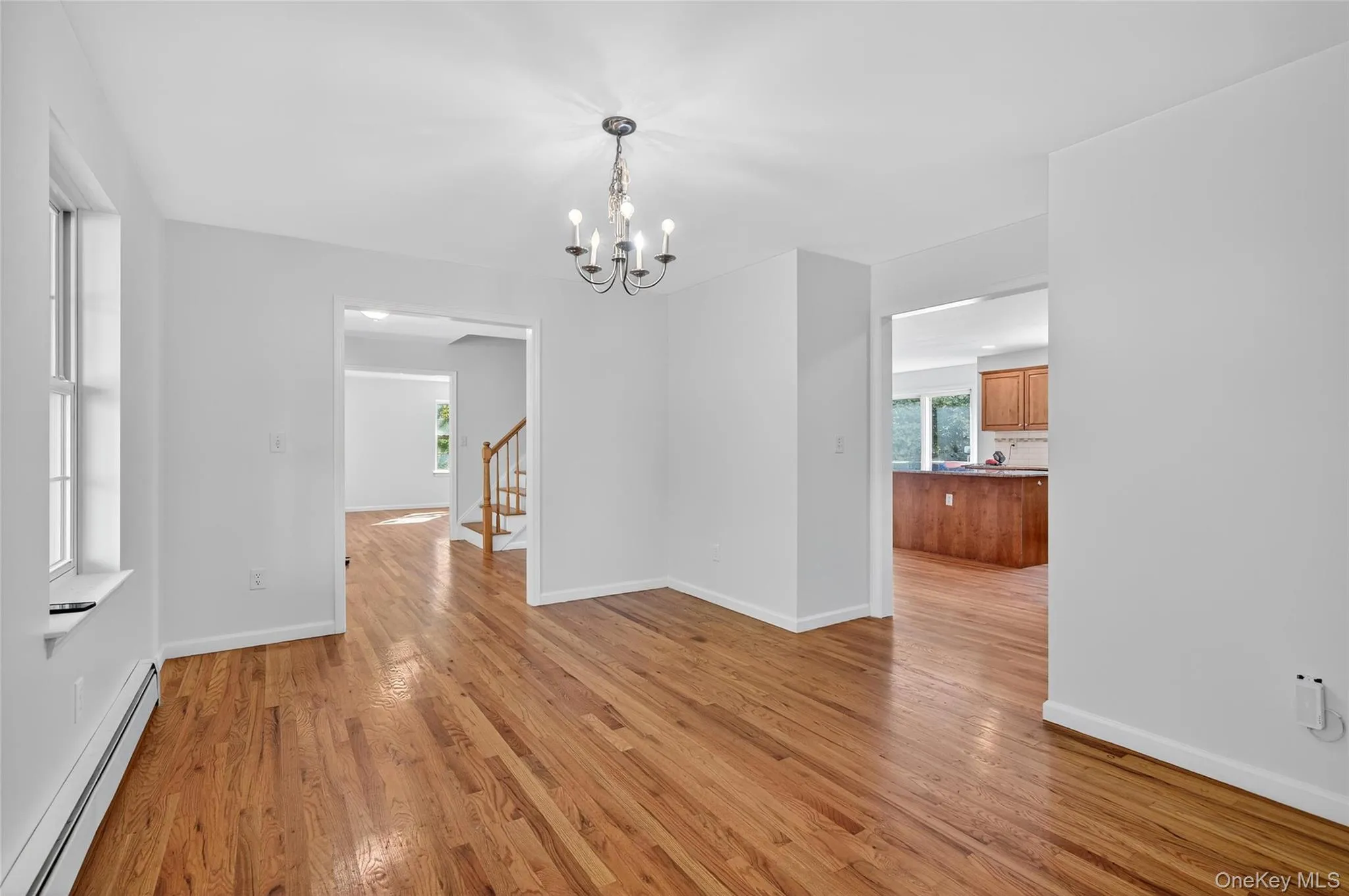 Unfurnished dining area with a baseboard heating unit, light wood-style floors, a chandelier, and stairway Unfurnished dining area with a baseboard heating unit, light wood-style floors, a chandelier, and stairway