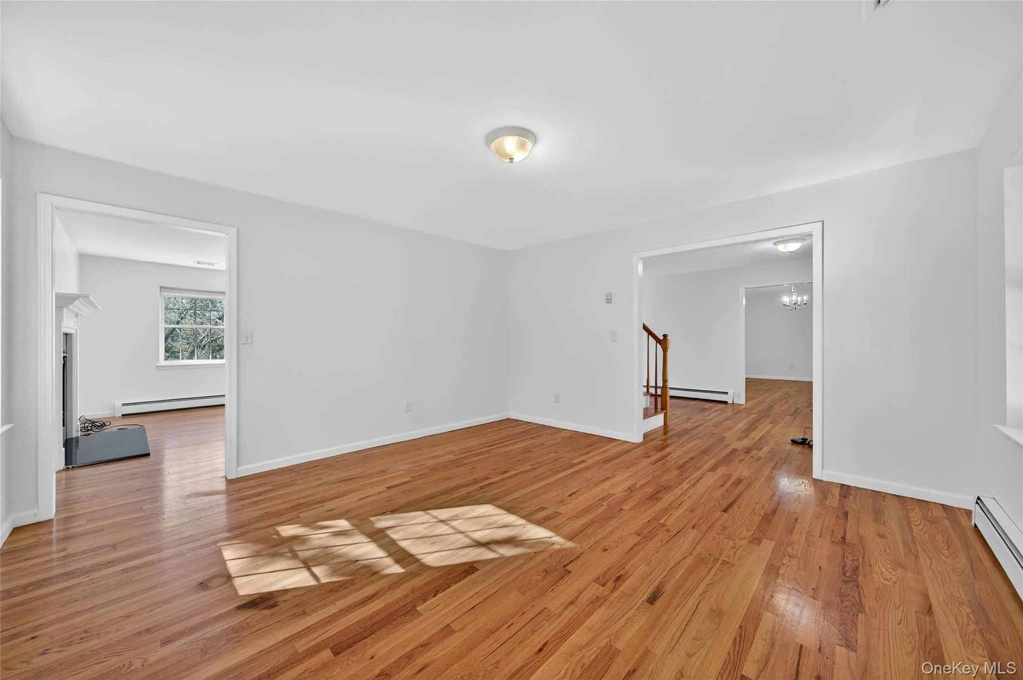 Unfurnished room featuring light wood-type flooring, a baseboard heating unit, a chandelier, and stairway Unfurnished room featuring light wood-type flooring, a baseboard heating unit, a chandelier, and stairway