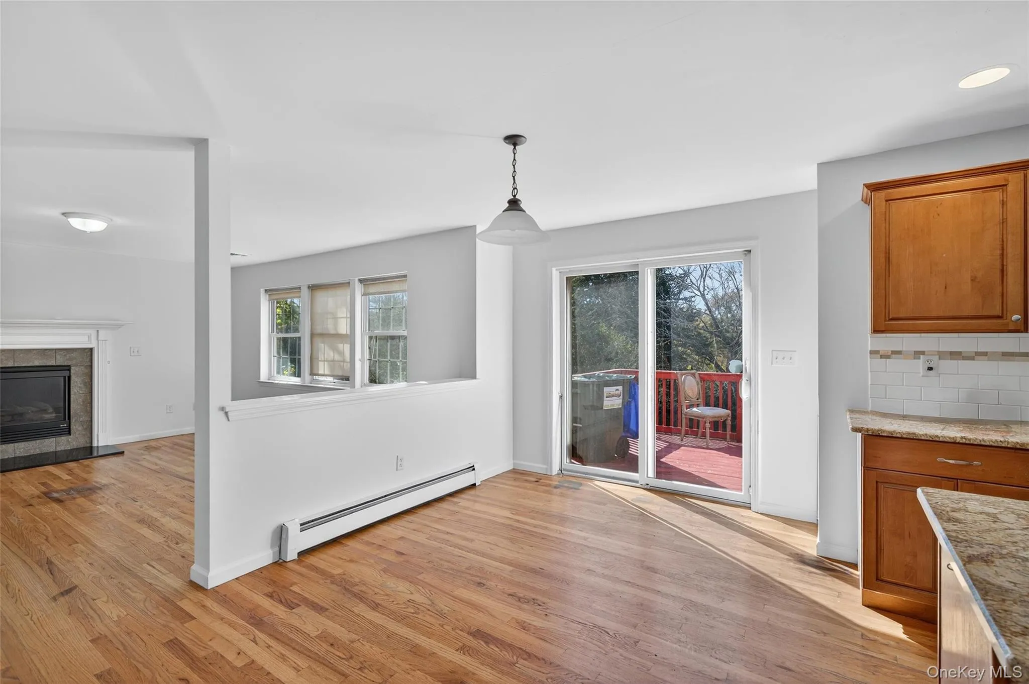 Unfurnished dining area featuring baseboard heating, light wood-style flooring, and a tiled fireplace Unfurnished dining area featuring baseboard heating, light wood-style flooring, and a tiled fireplace